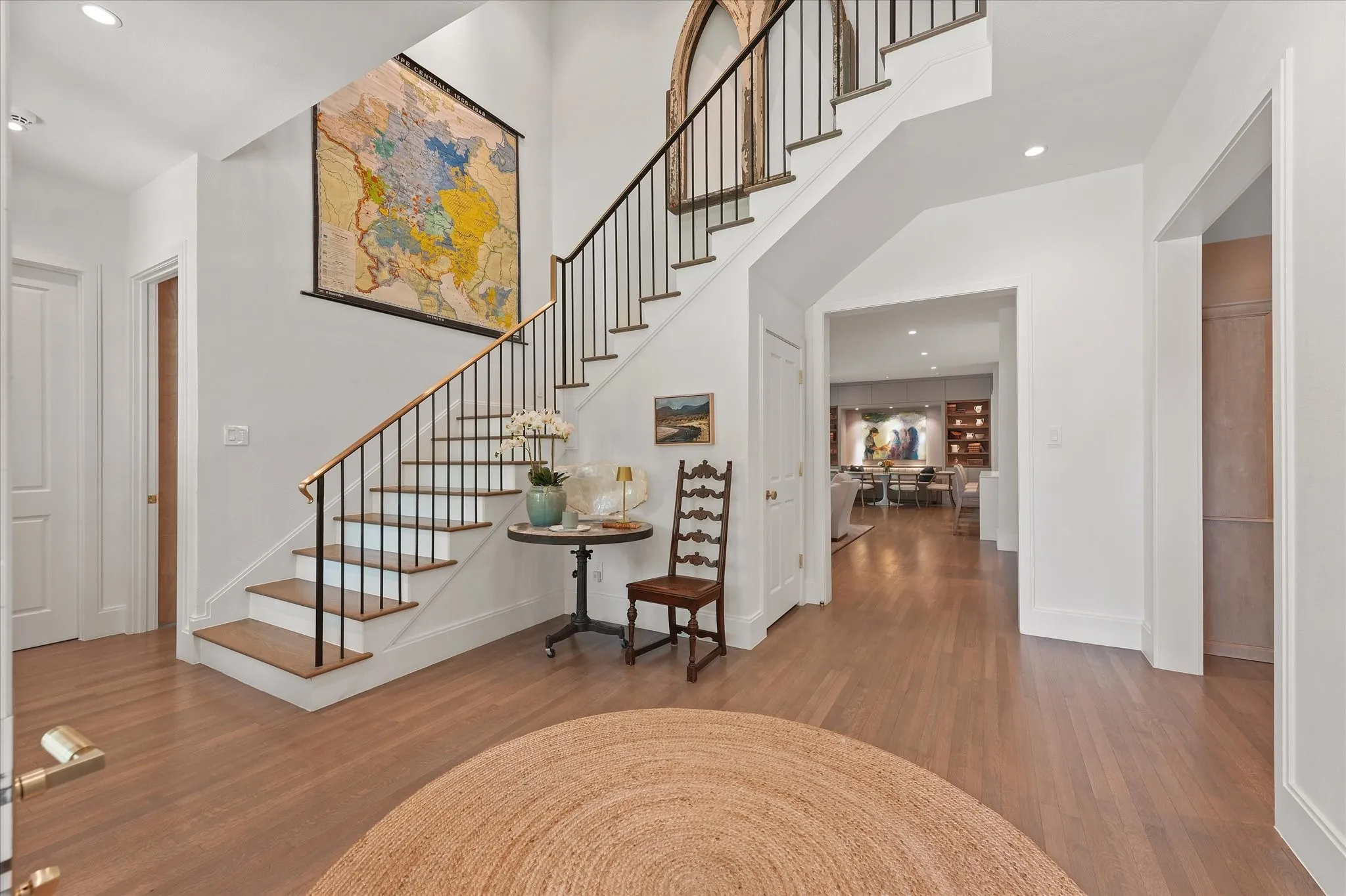 Wood stair treads pair with slender black balusters and a gold-toned handrail, while an open hallway leads toward the living room.