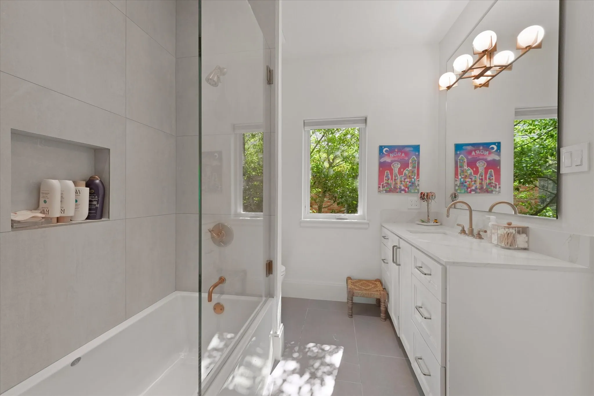 A glass panel borders the tub and shower with large format tile, and adjoining walk-in closet.