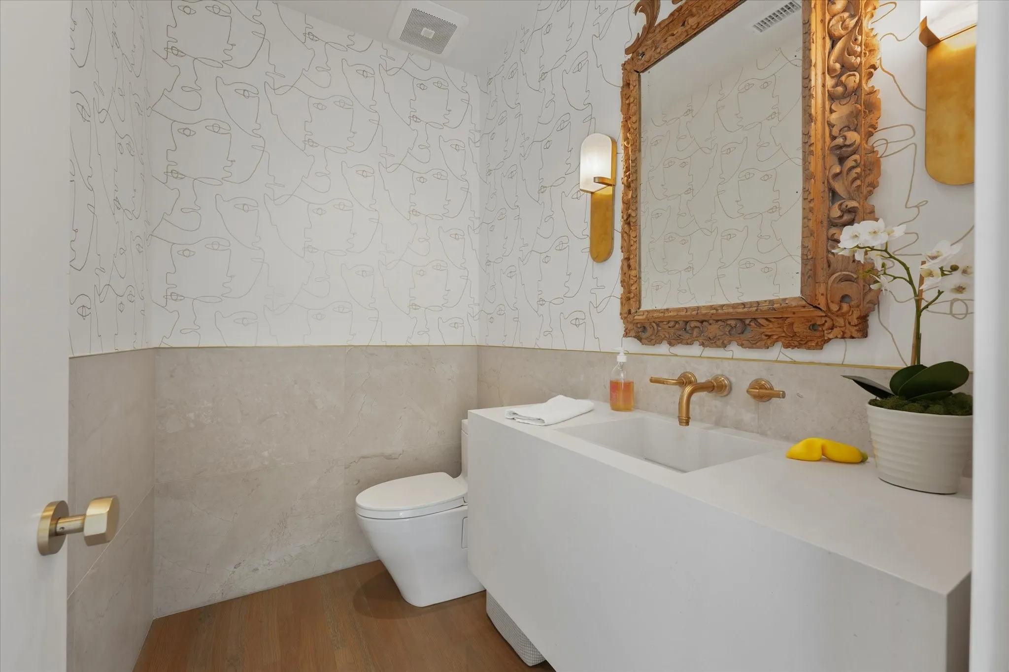 A carved gold-toned mirror and wall-mounted faucet over a white vanity.