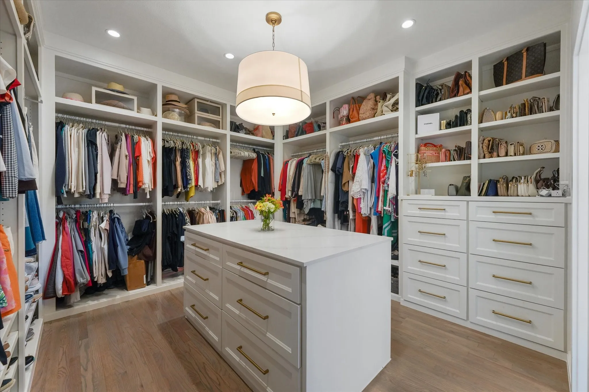 Built-ins combine double hanging rods, open shelving and drawers around a center island beneath a drum pendant.