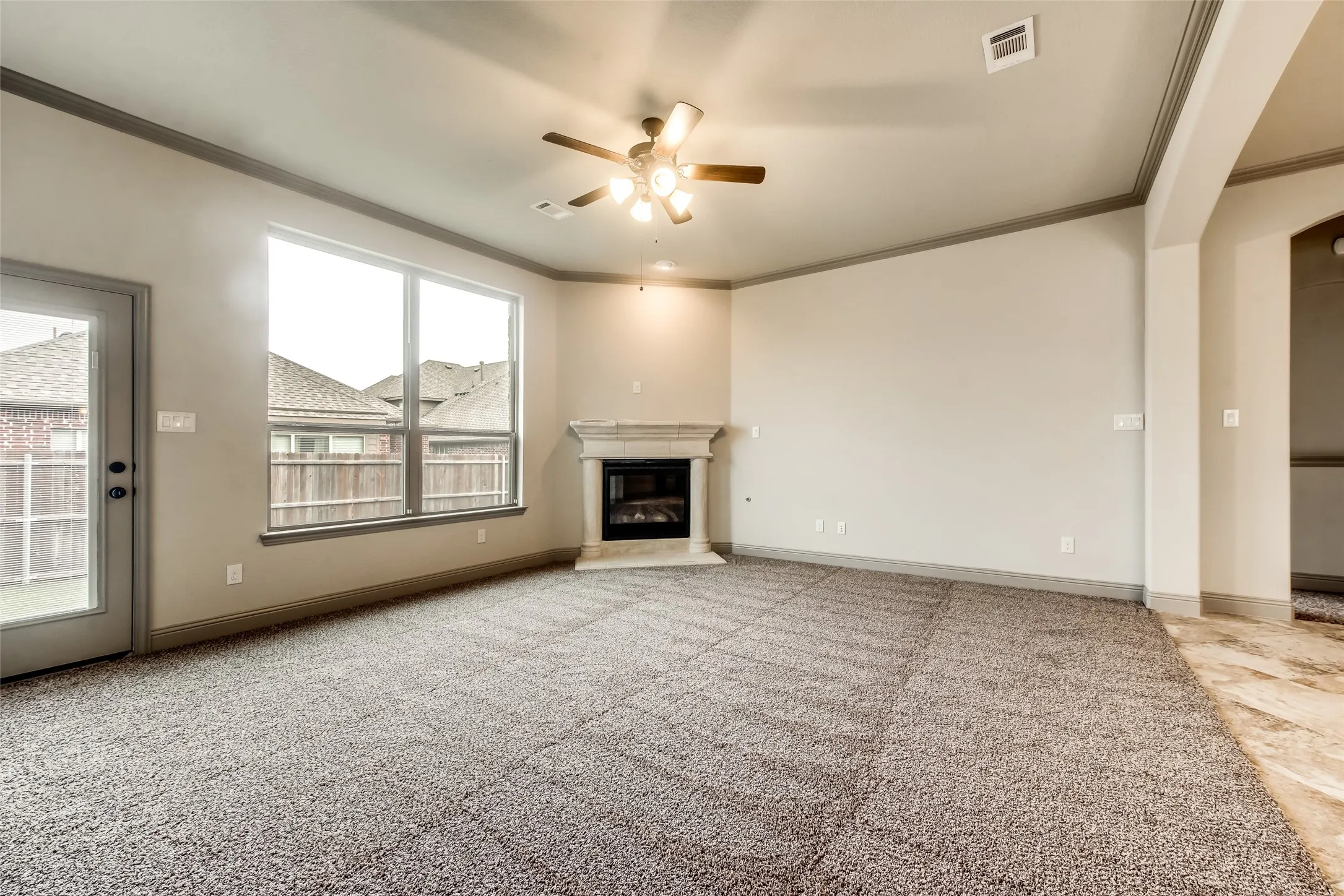 Spacious living area featuring neutral carpeting, a built-in fireplace with a stone surround, and multiple windows