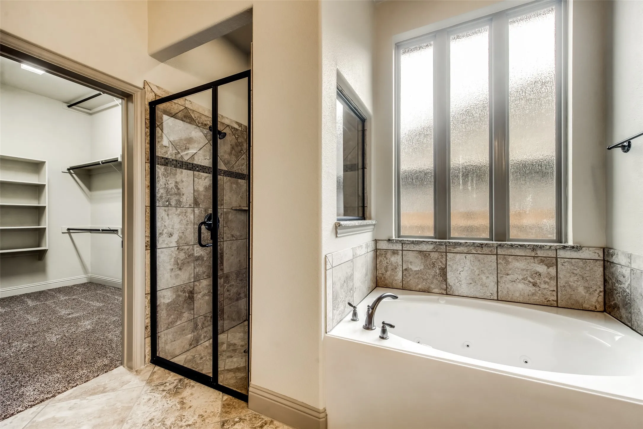Built-in corner bathtub, tiled shower enclosure with dark-framed glass door, and a separate walk-in closet with built-in shelving