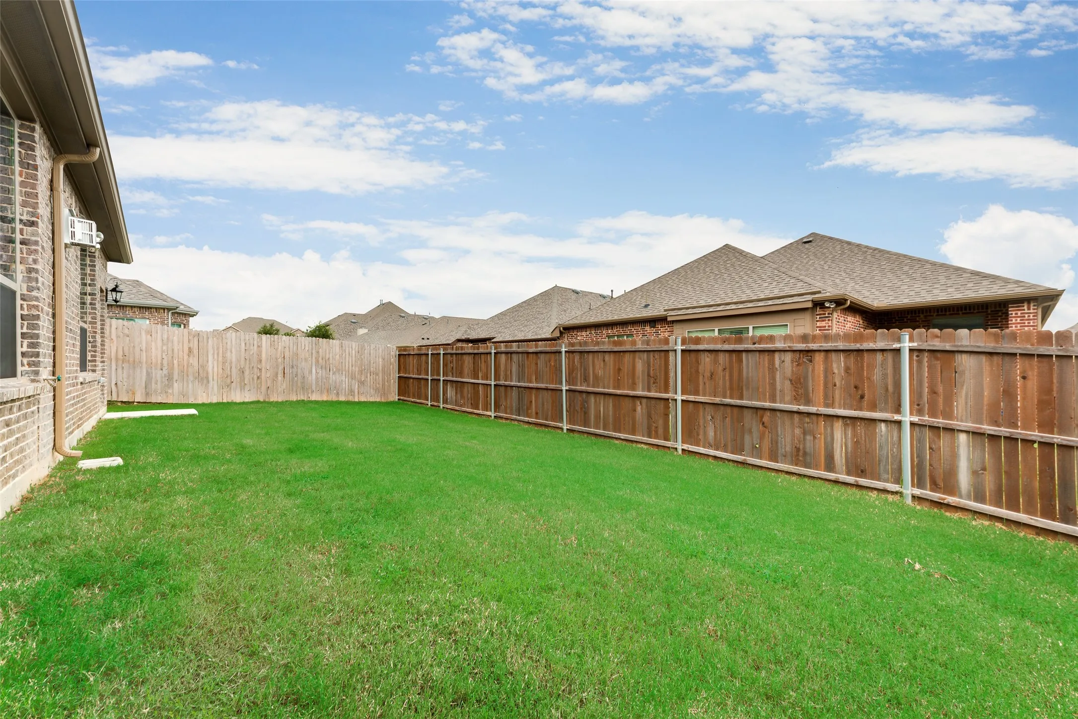 Expansive backyard with a manicured lawn, full privacy fencing, and a brick exterior