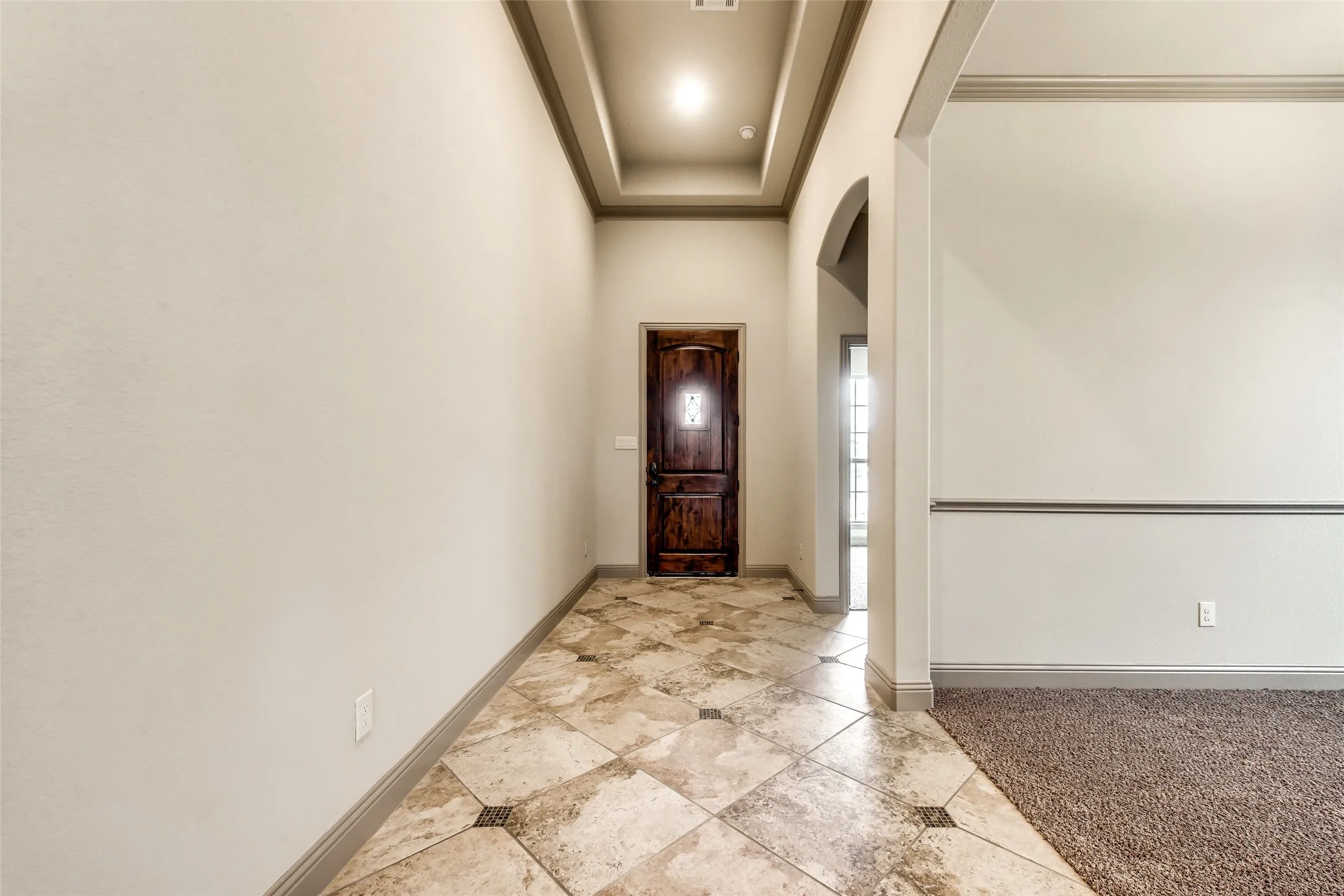 Tray ceiling with recessed lighting, stone tile flooring, wood entry door, arched doorway, and carpeted area