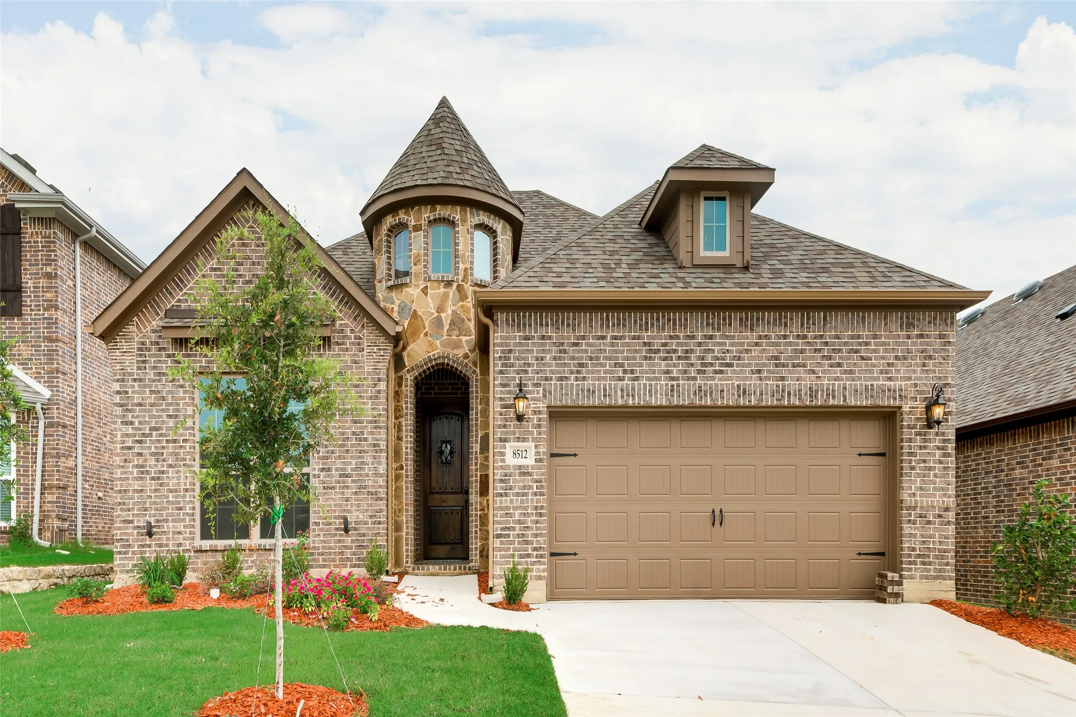 Brick exterior with stone accents, turret detail, dormer window, two-car garage, and established landscaping