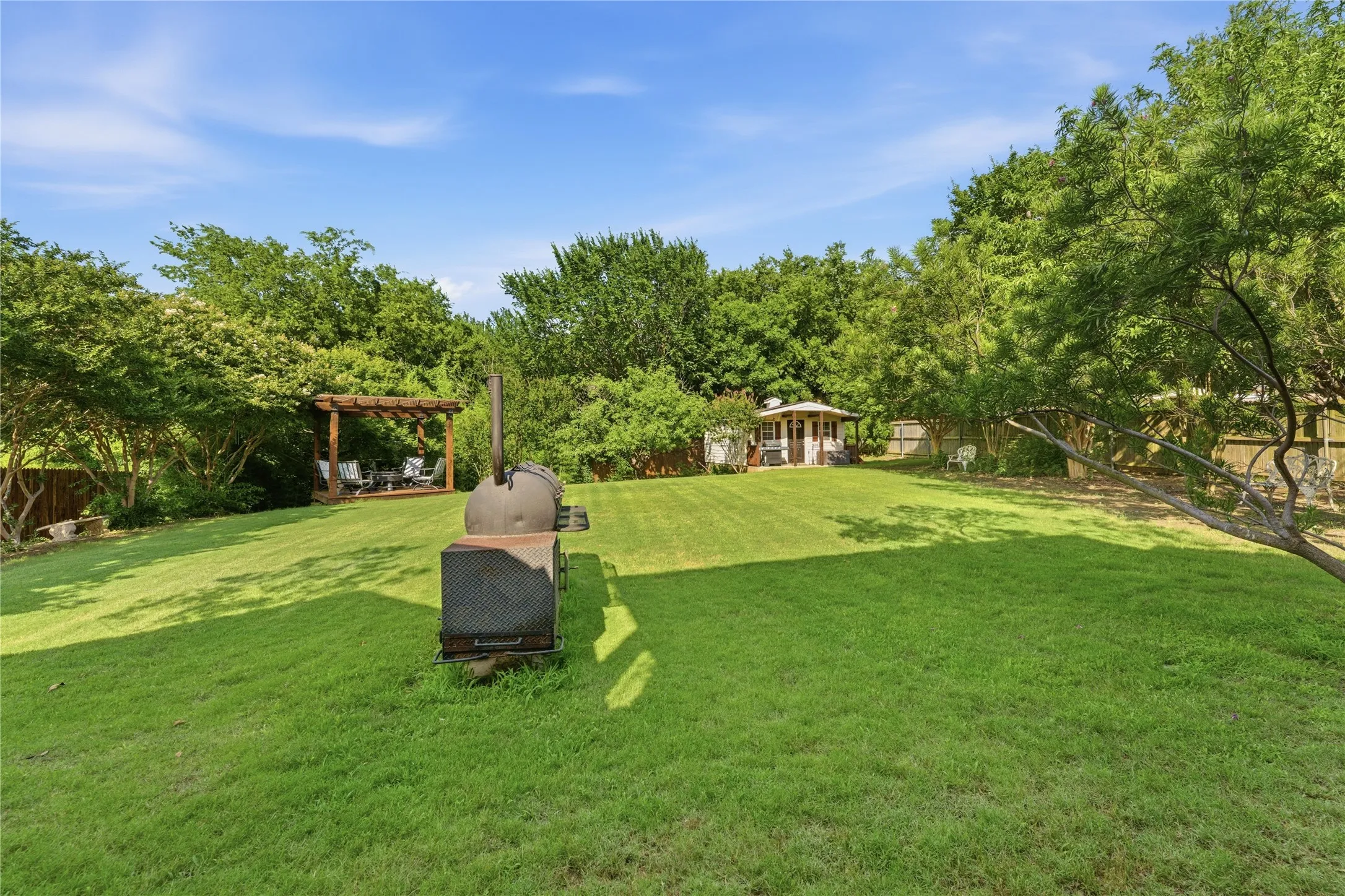 Expansive backyard featuring a manicured lawn, mature trees, a wooden pergola, and a detached gazebo