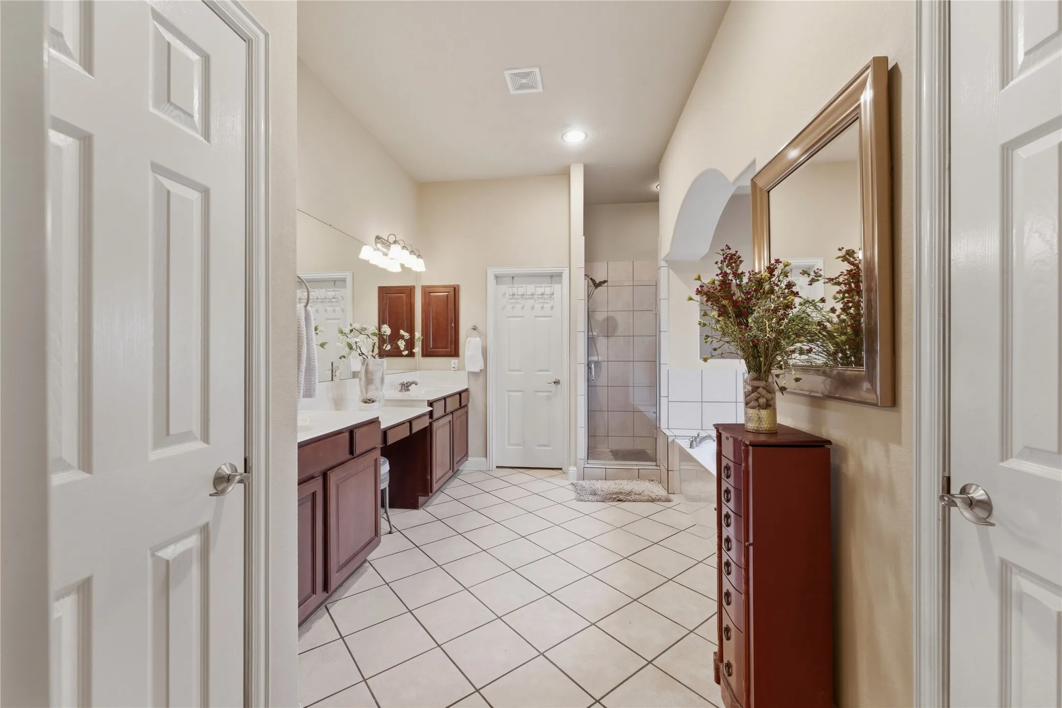 Bathroom featuring vaulted ceilings, dual vanities with white countertops, tiled flooring, a glass-enclosed shower, and a built-in soaking tub