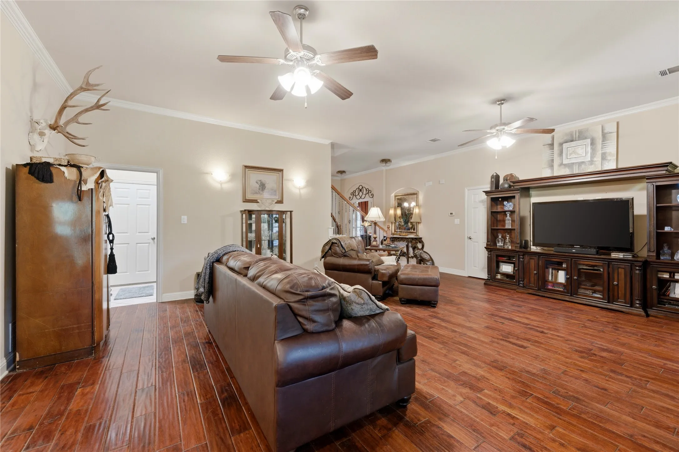 Open-concept room featuring wood-finish flooring, two ceiling fans, and a built-in media cabinet
