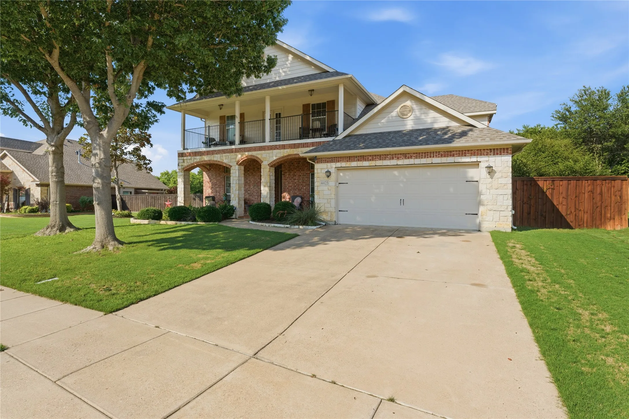 Two-story facade with stone and brick accents, covered front porch with arched entries, second-level balcony, two-car garage, and concrete driveway