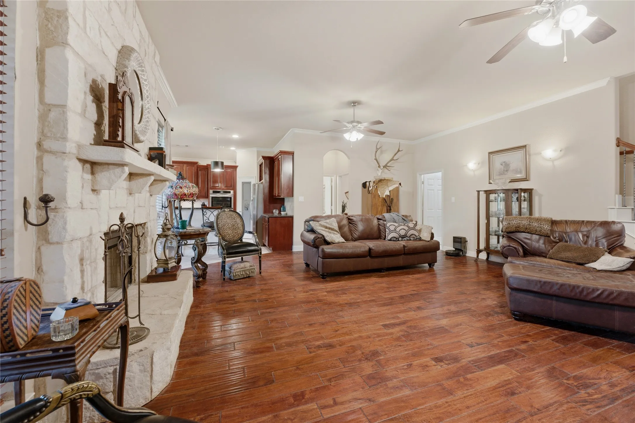 Spacious living area featuring wood-finish flooring, a stone fireplace, and ceiling fans