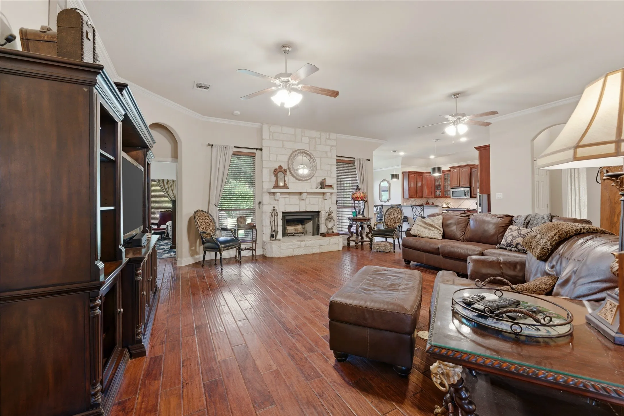 Hardwood flooring throughout, stone-clad fireplace with mantel, ceiling fans, arched doorways, and crown molding
