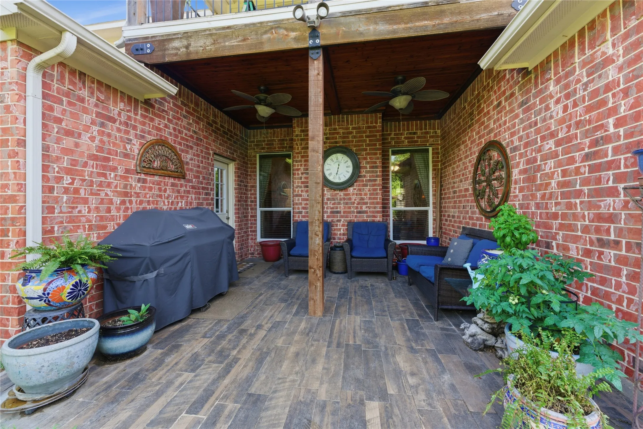 Covered patio with brick exterior, wood-finish flooring, and a wood-paneled ceiling featuring two ceiling fans