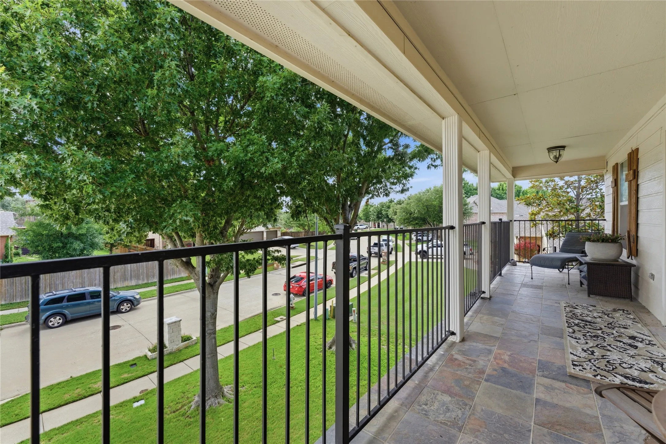 Covered balcony featuring tile flooring, white columns, black metal railing, and wood shutters