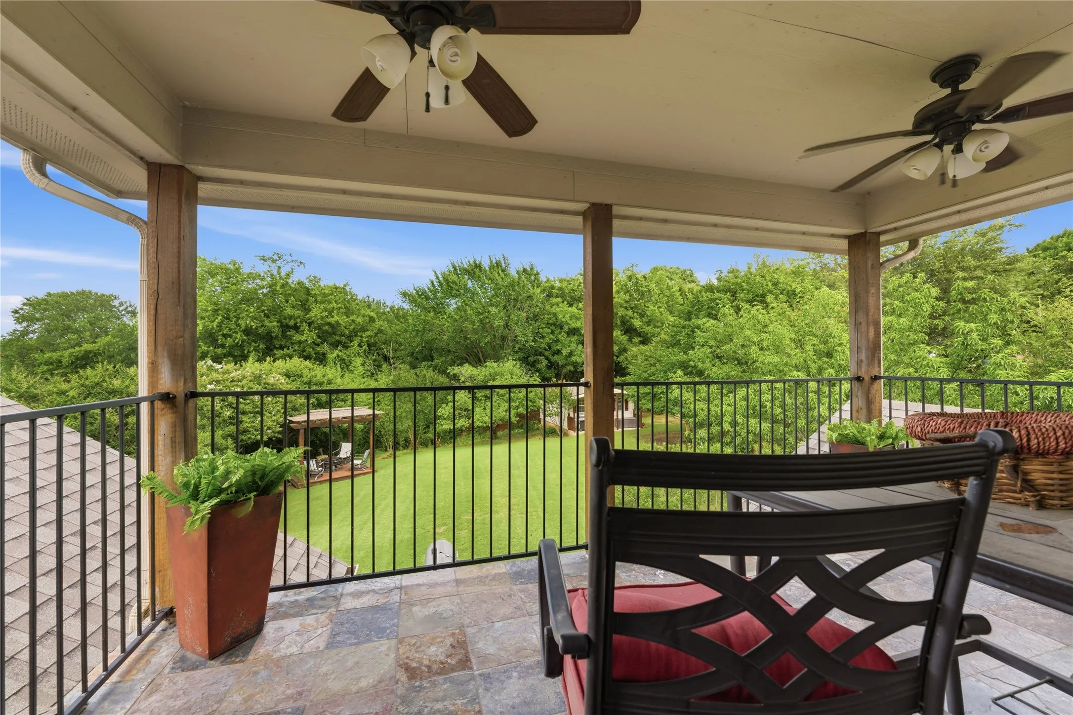 Covered outdoor patio with a tiled floor, wood support pillars, and ceiling fans
