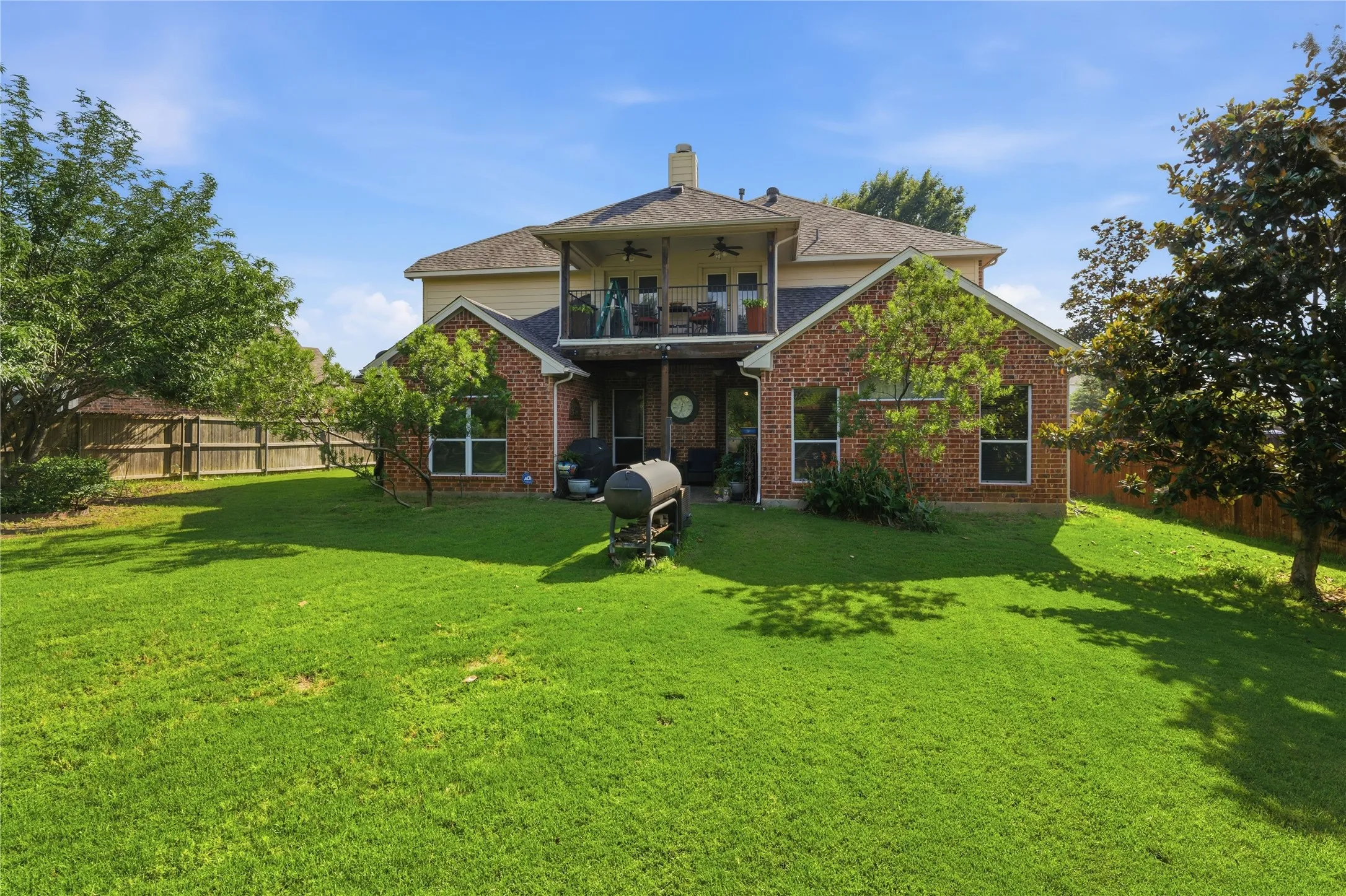 Expansive green lawn with a two-story brick and siding exterior, featuring a second-story balcony and ground-level patio