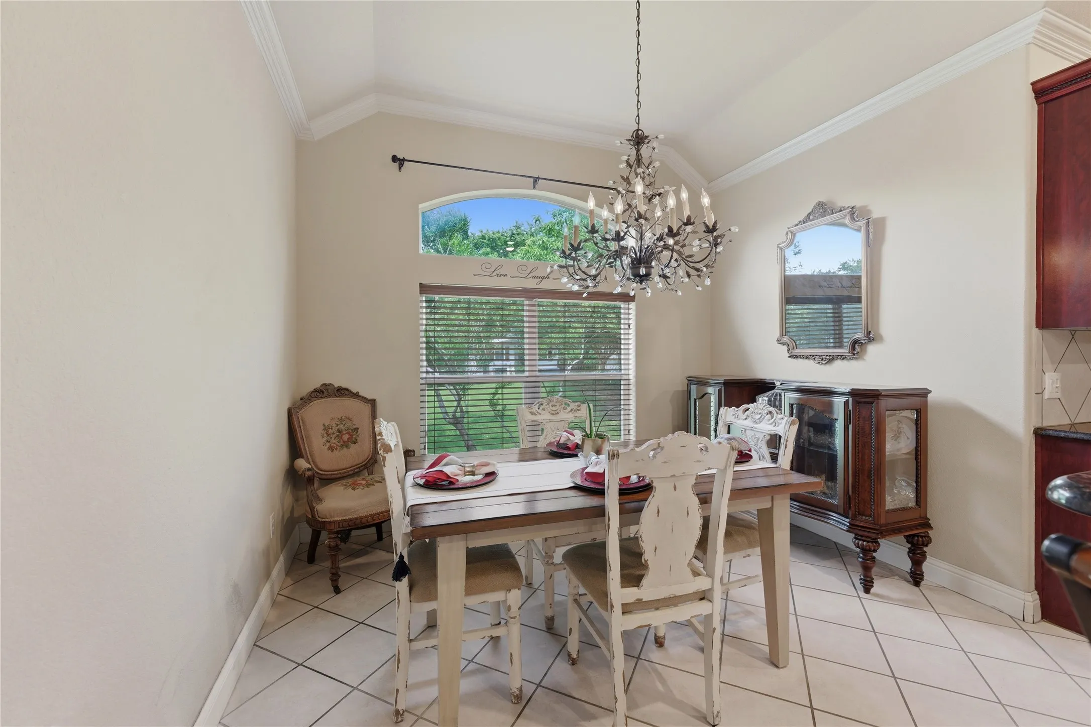 Vaulted ceiling with crown molding, arched transom window, ceramic tile flooring, and elegant chandelier