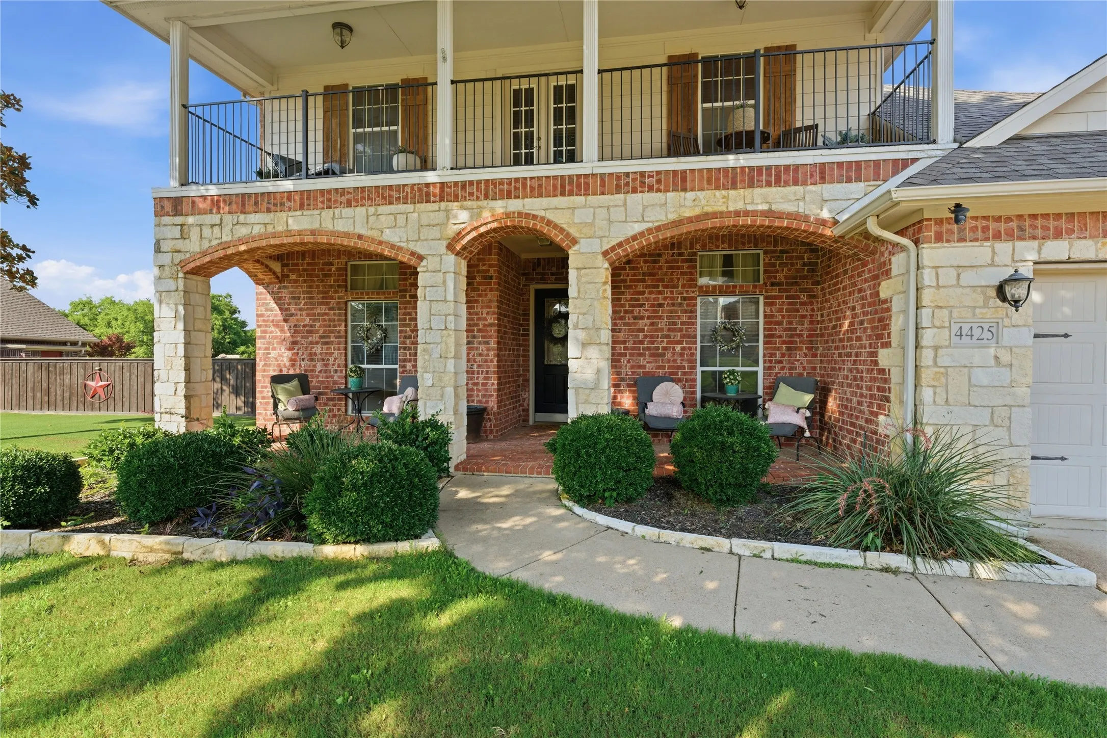 Brick and stone exterior with an arched entry porch, second-story balcony with metal railing, and an attached garage