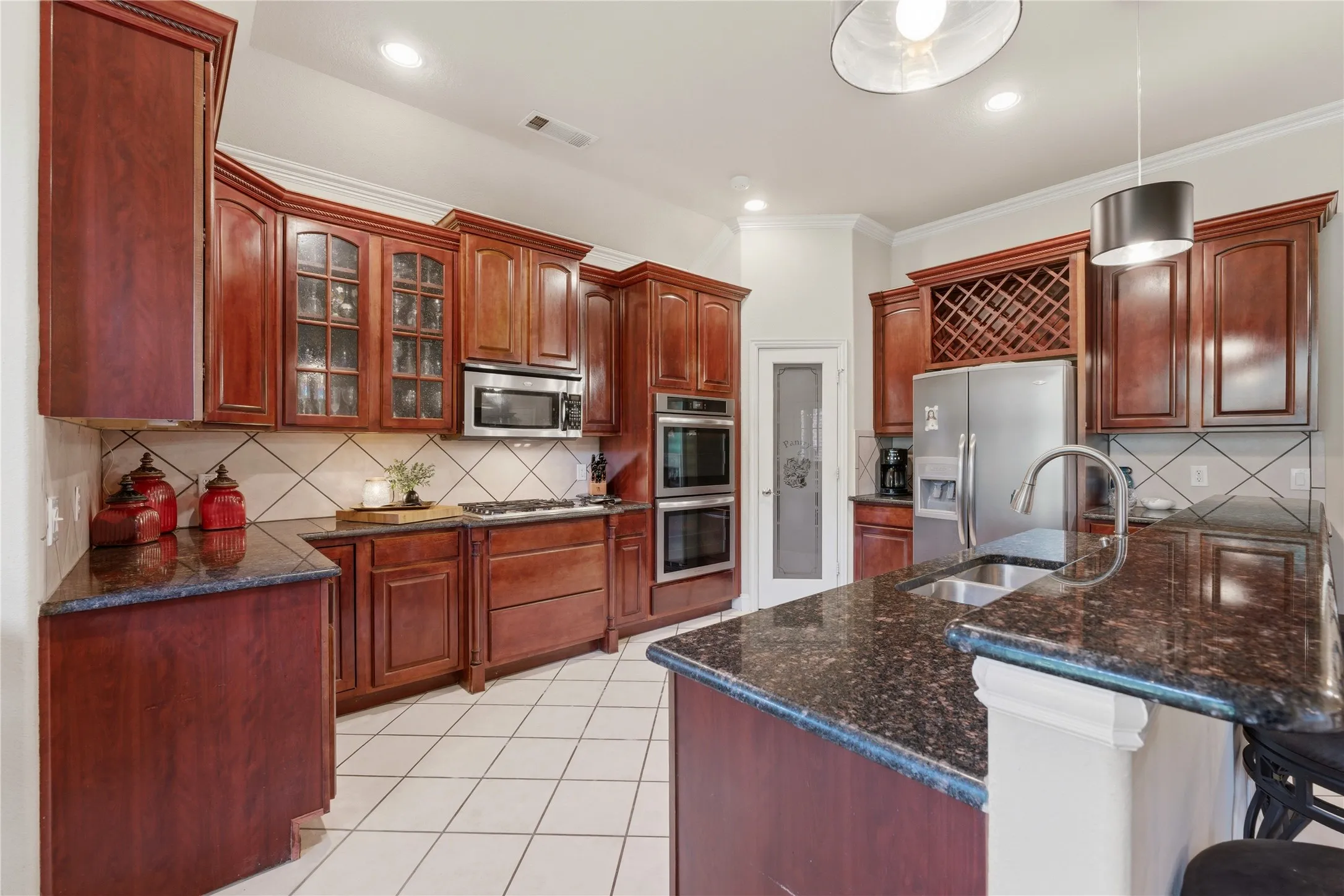 Kitchen featuring wood cabinetry, dark speckled countertops, stainless steel appliances, tile flooring, and a built-in wine rack