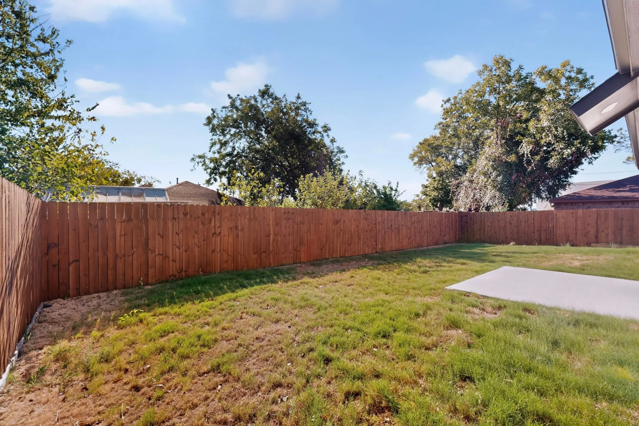 Spacious backyard featuring a wood privacy fence, concrete patio, and mature perimeter trees
