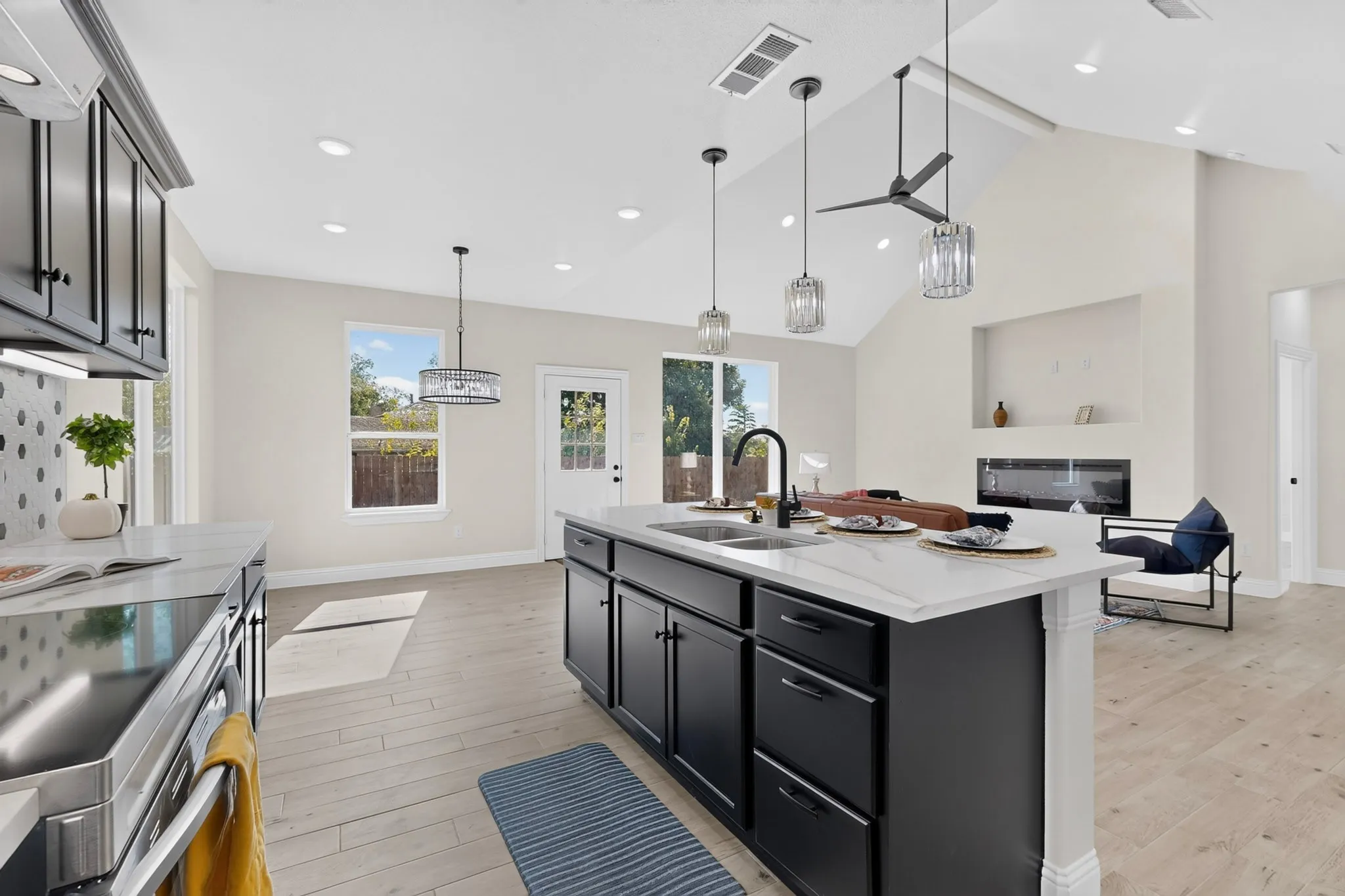 Stunning open-concept kitchen featuring a large center island with white quartz countertop, black cabinetry with hardware accents, and stainless steel appliances