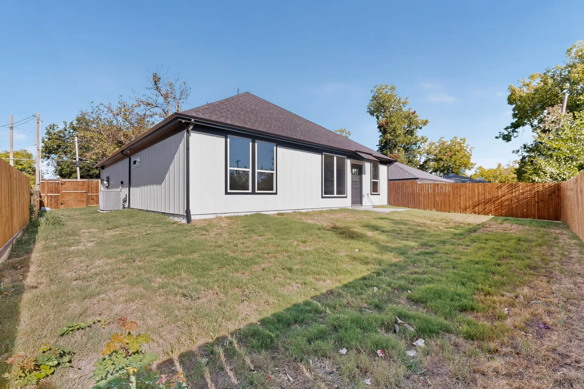 Expansive grass area with a newly installed wood privacy fence, featuring a contemporary exterior with multiple windows and a rear entry door