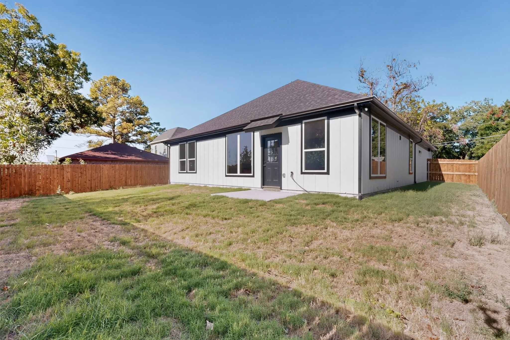 Expansive backyard featuring a partial privacy fence, a concrete patio, and a dark shingle roof