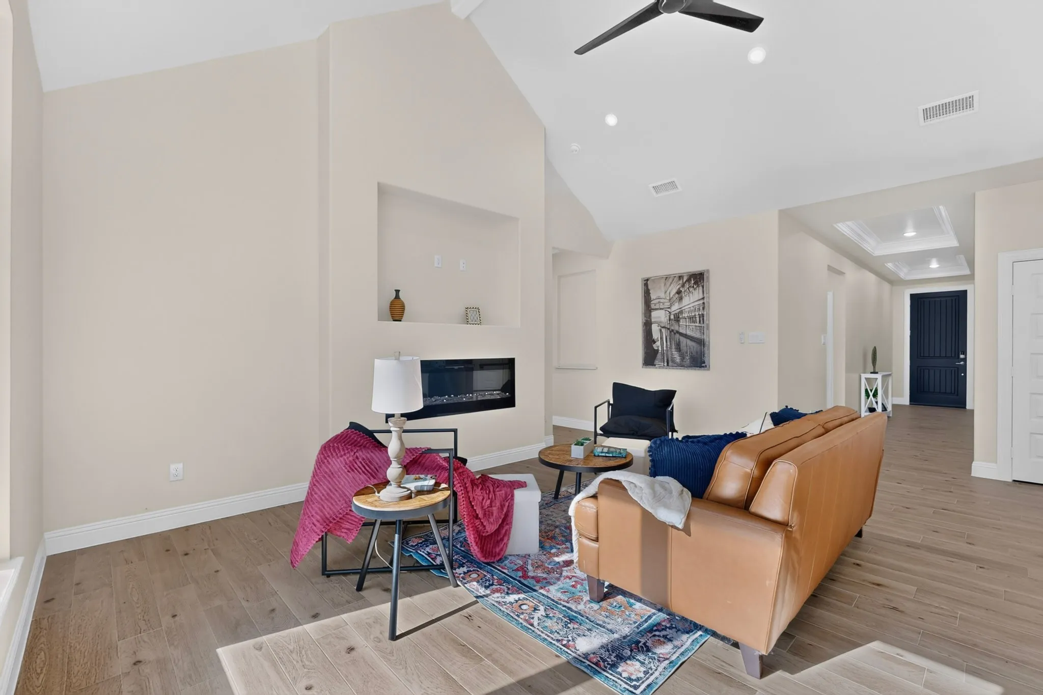 Vaulted ceiling with a contemporary ceiling fan, wood-finish flooring, recessed lighting, built-in electric fireplace, and a tray ceiling in the hallway