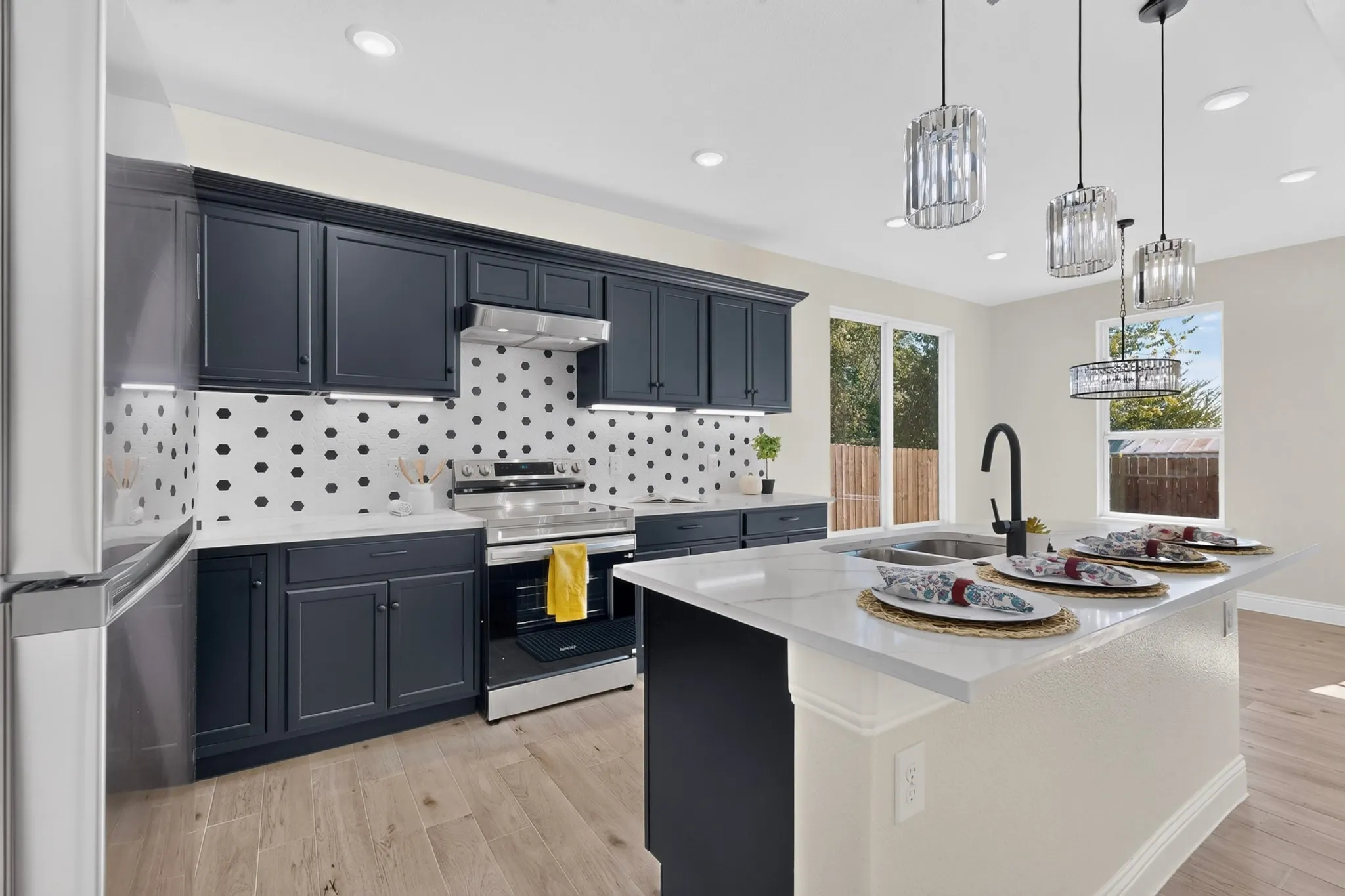 Modern kitchen featuring dark cabinetry, stainless steel appliances, a center island with sink, polished countertops, and wood-finish flooring