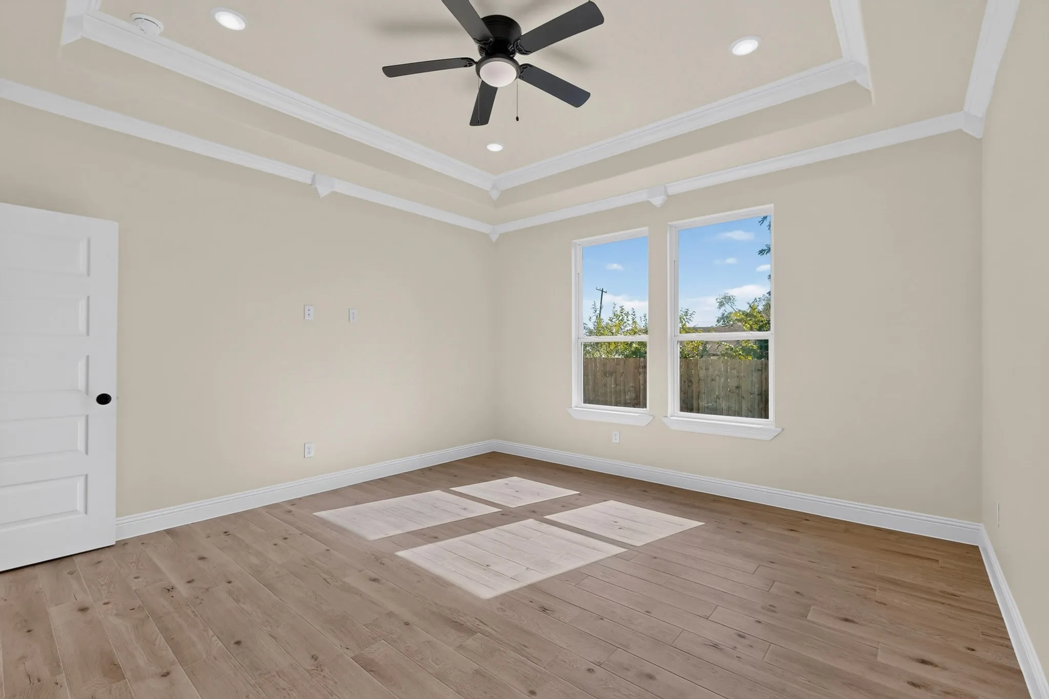 Tray ceiling with recessed lighting and a ceiling fan, complemented by two windows and wood-finish flooring