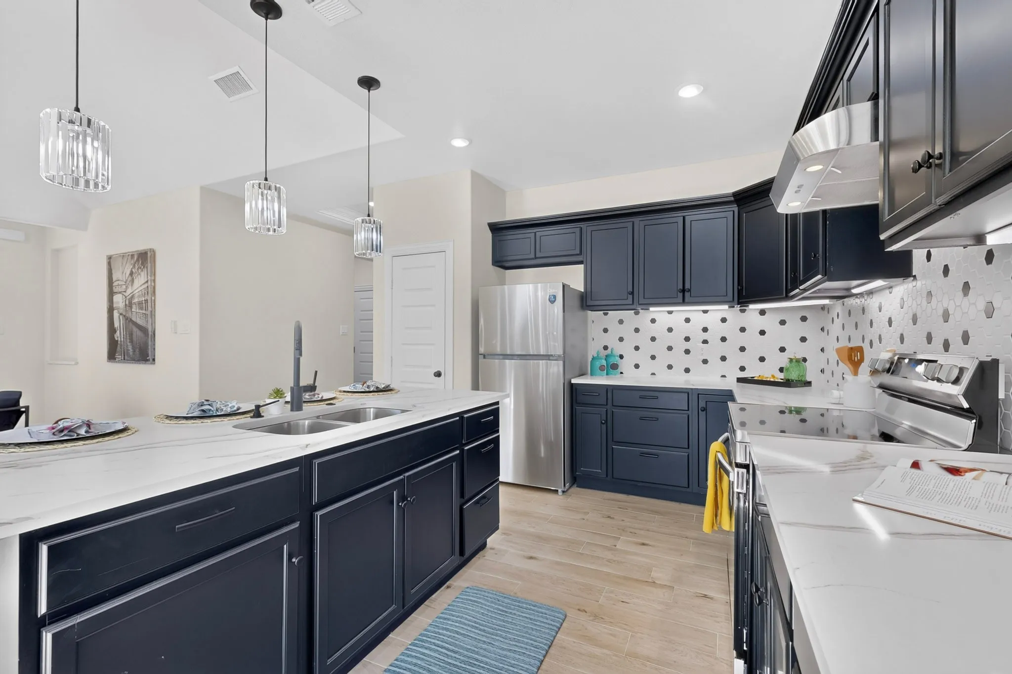 Kitchen featuring dark cabinetry, stainless steel appliances, a center island with double sinks, light countertops, and wood-finish flooring