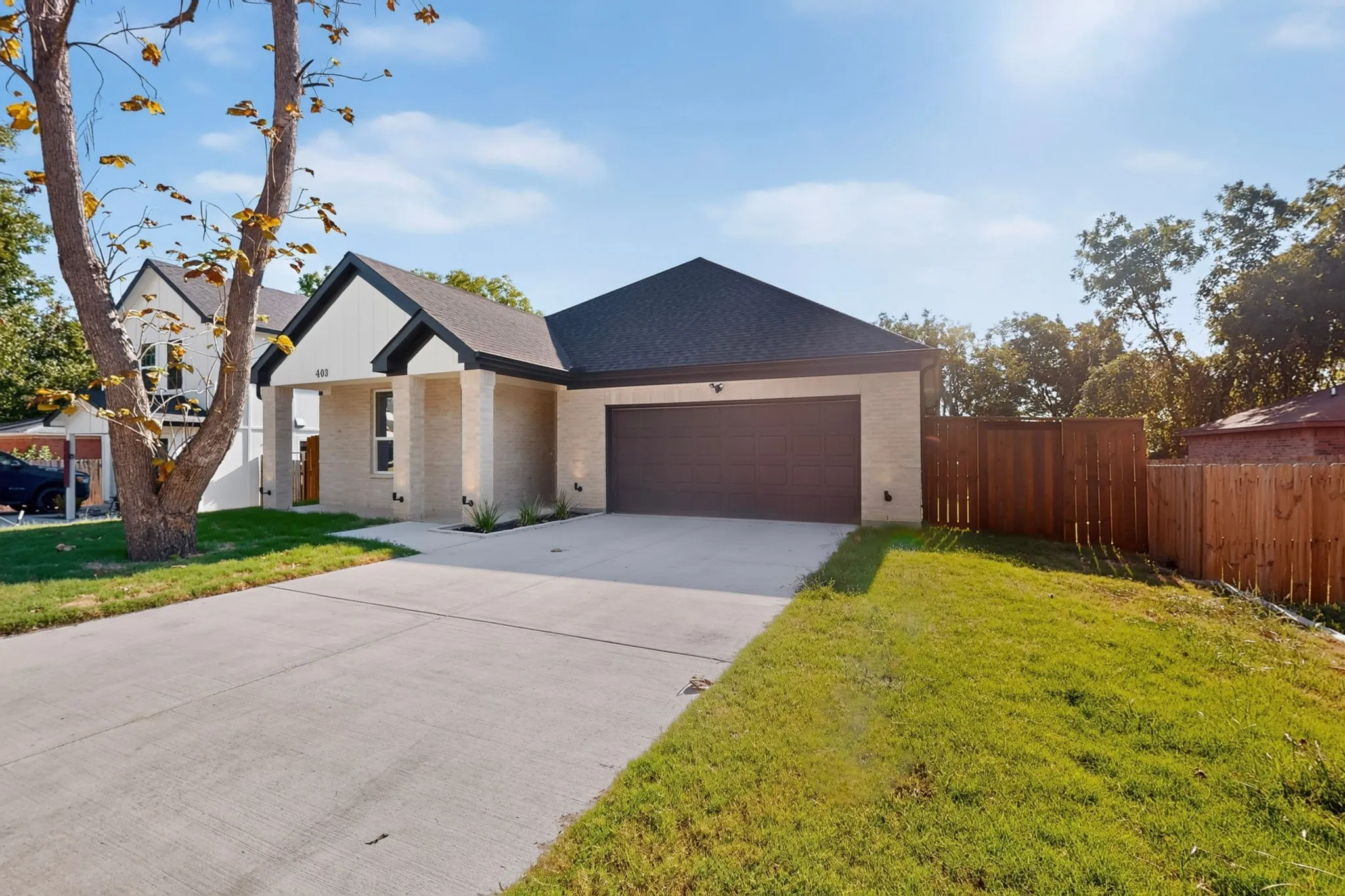 Contemporary exterior featuring light brick, dark trim accents, a two-car garage, and a wood privacy fence