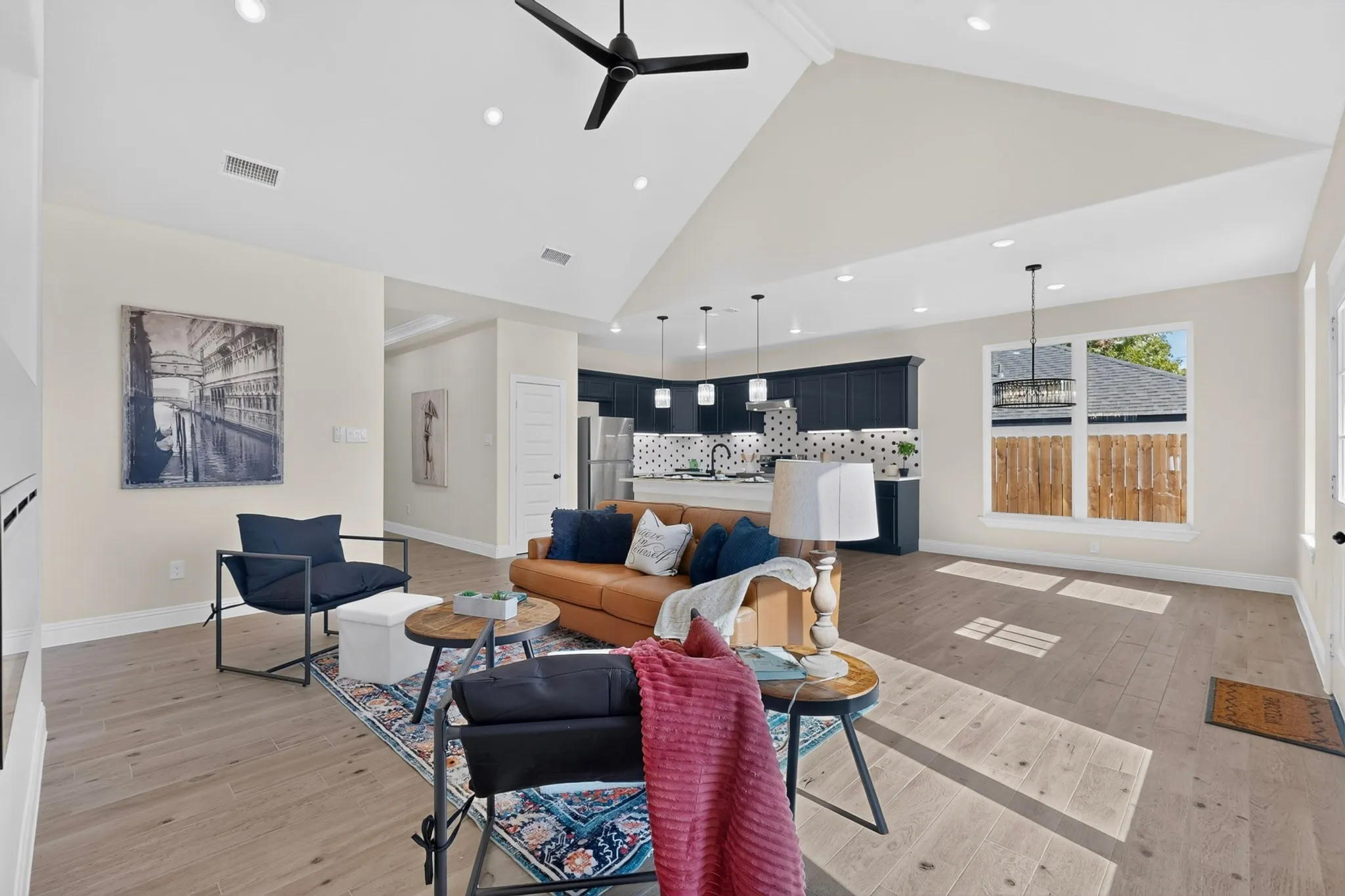 Vaulted ceiling, recessed lighting, wood-finish flooring, kitchen with dark cabinetry, and a large window