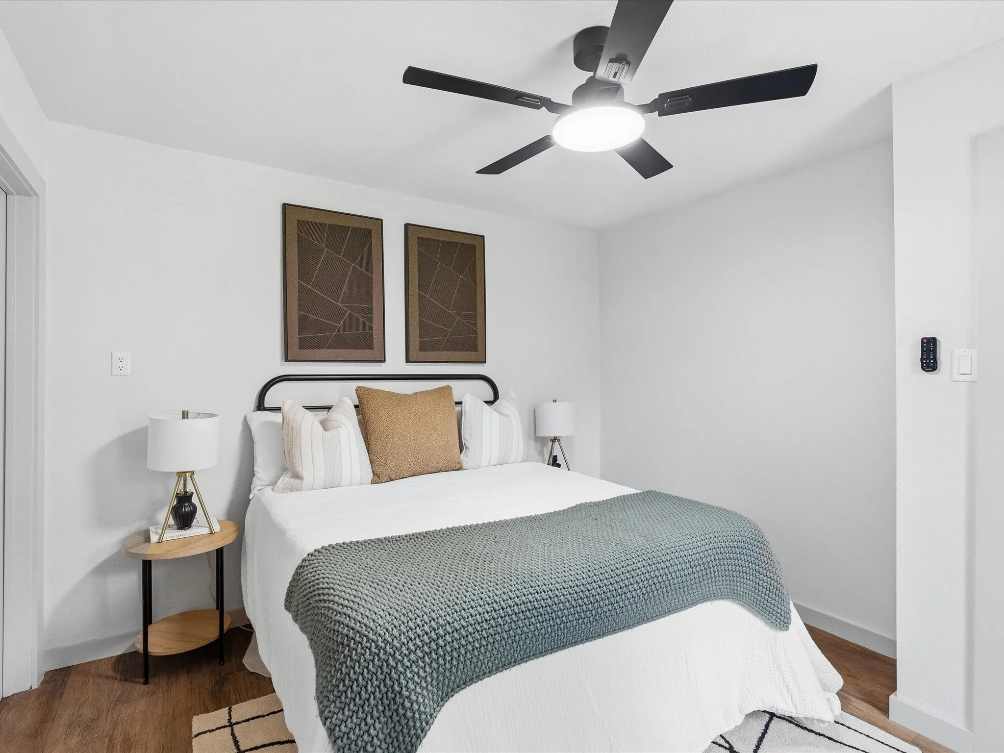 White walls, wood-finish flooring, and a ceiling fan with integrated lighting