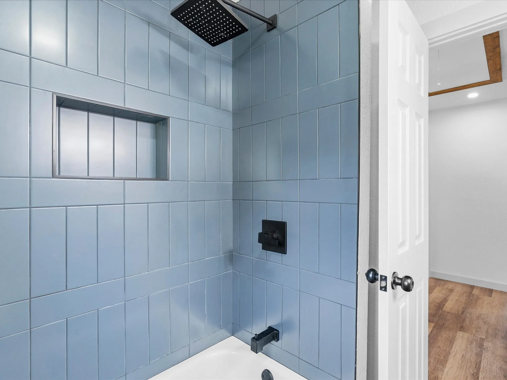 Shower with blue subway tile surround, built-in recessed niche, matte black rain shower head, and coordinating fixtures
