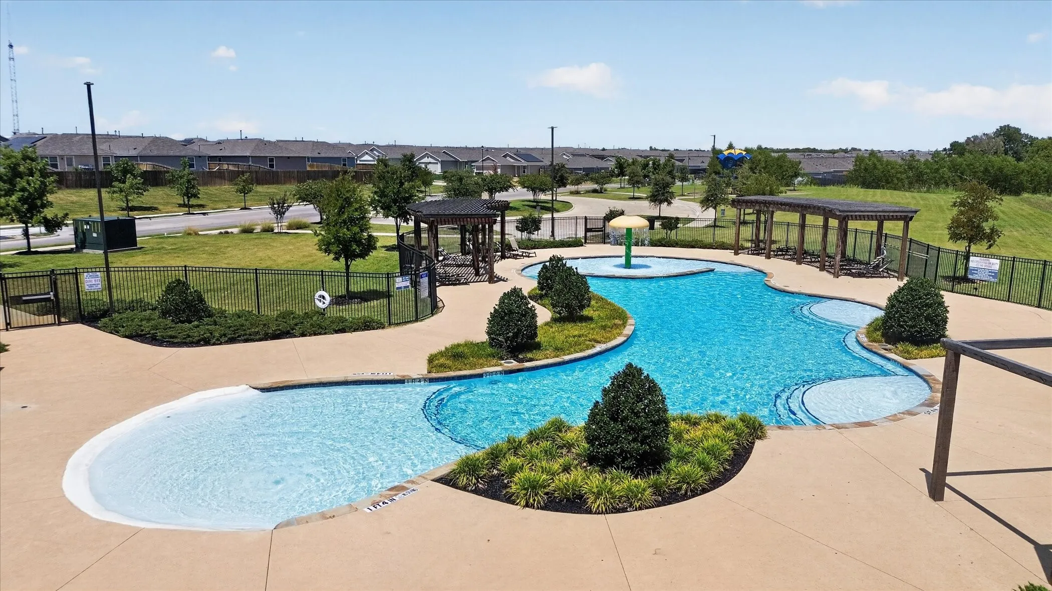 Community pool with integrated splash pad, adjacent clubhouse, and landscaped green space