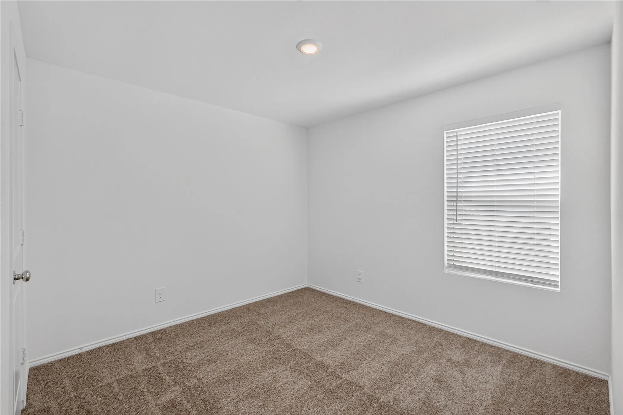 Recessed ceiling lighting, neutral carpet flooring, white walls, and a window with blinds