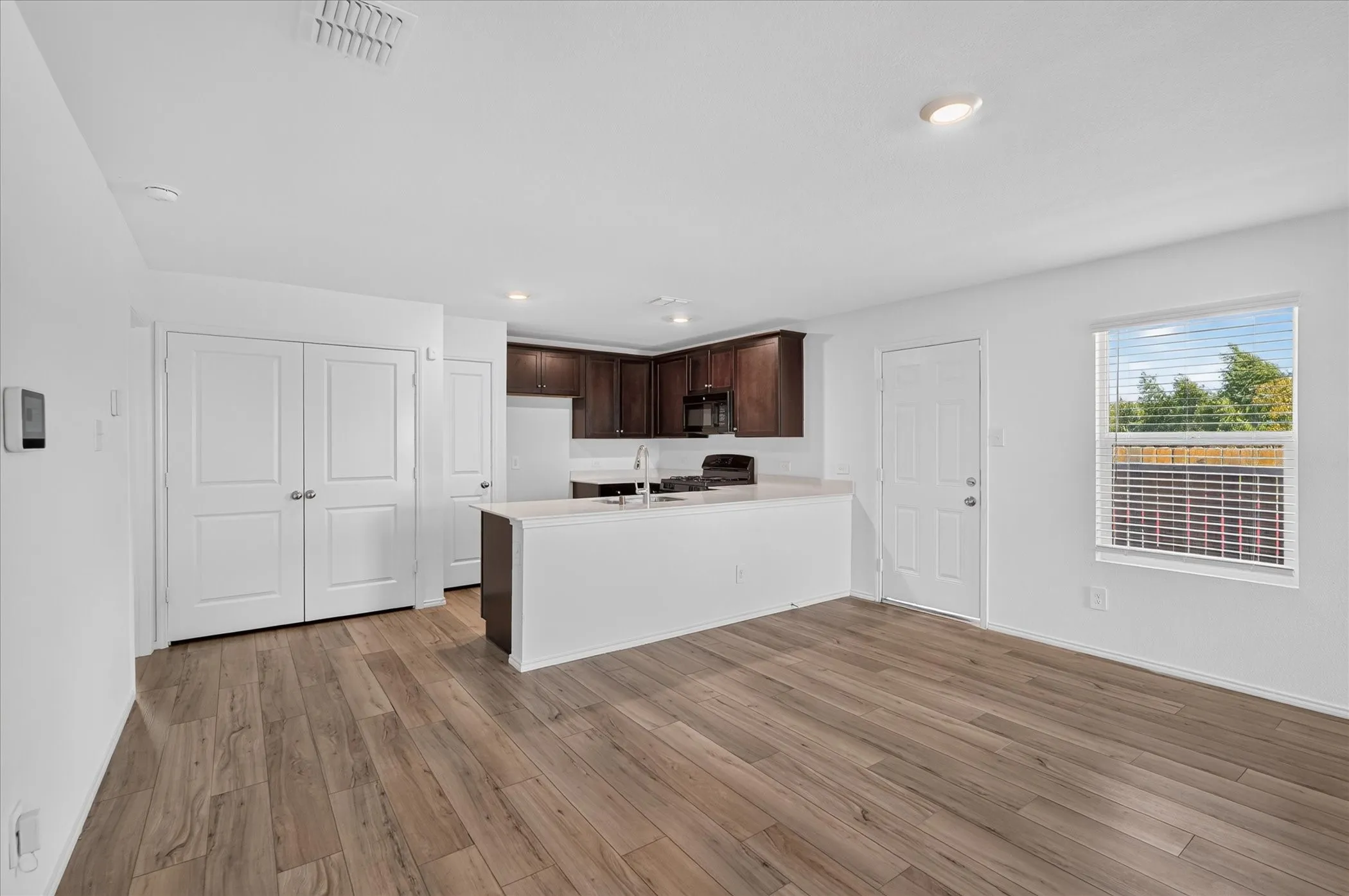 Open-concept kitchen and living area featuring wood-finish flooring, white walls, dark wood cabinetry, and a kitchen island with a white countertop