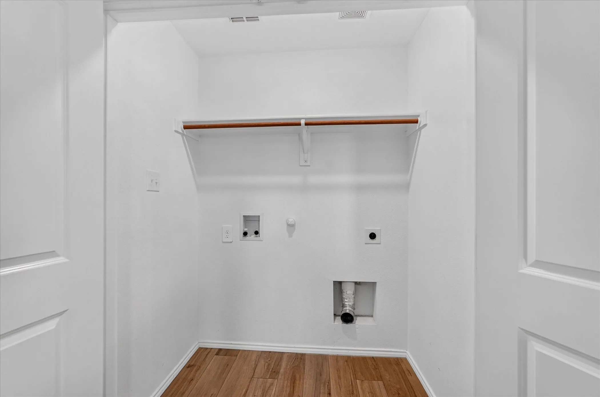 Dedicated laundry area featuring wood-finish flooring, a built-in shelf, and a clothing rod
