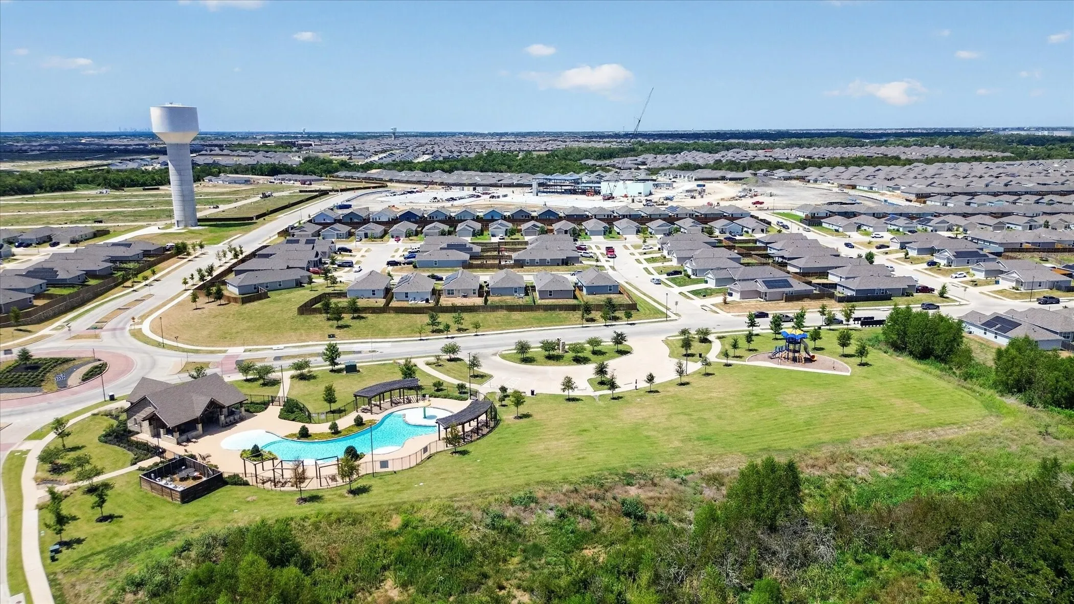 Community pool with integrated splash pad, adjacent clubhouse, and landscaped green space