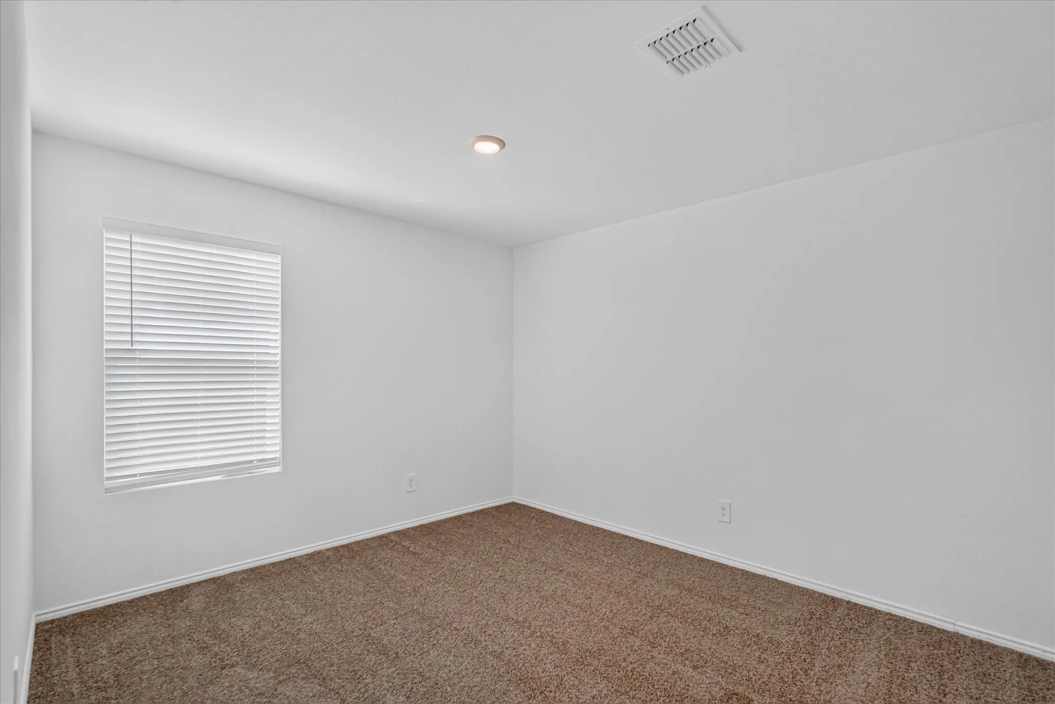 Light-filled room featuring neutral carpeting, white walls, a single window with blinds, and recessed lighting