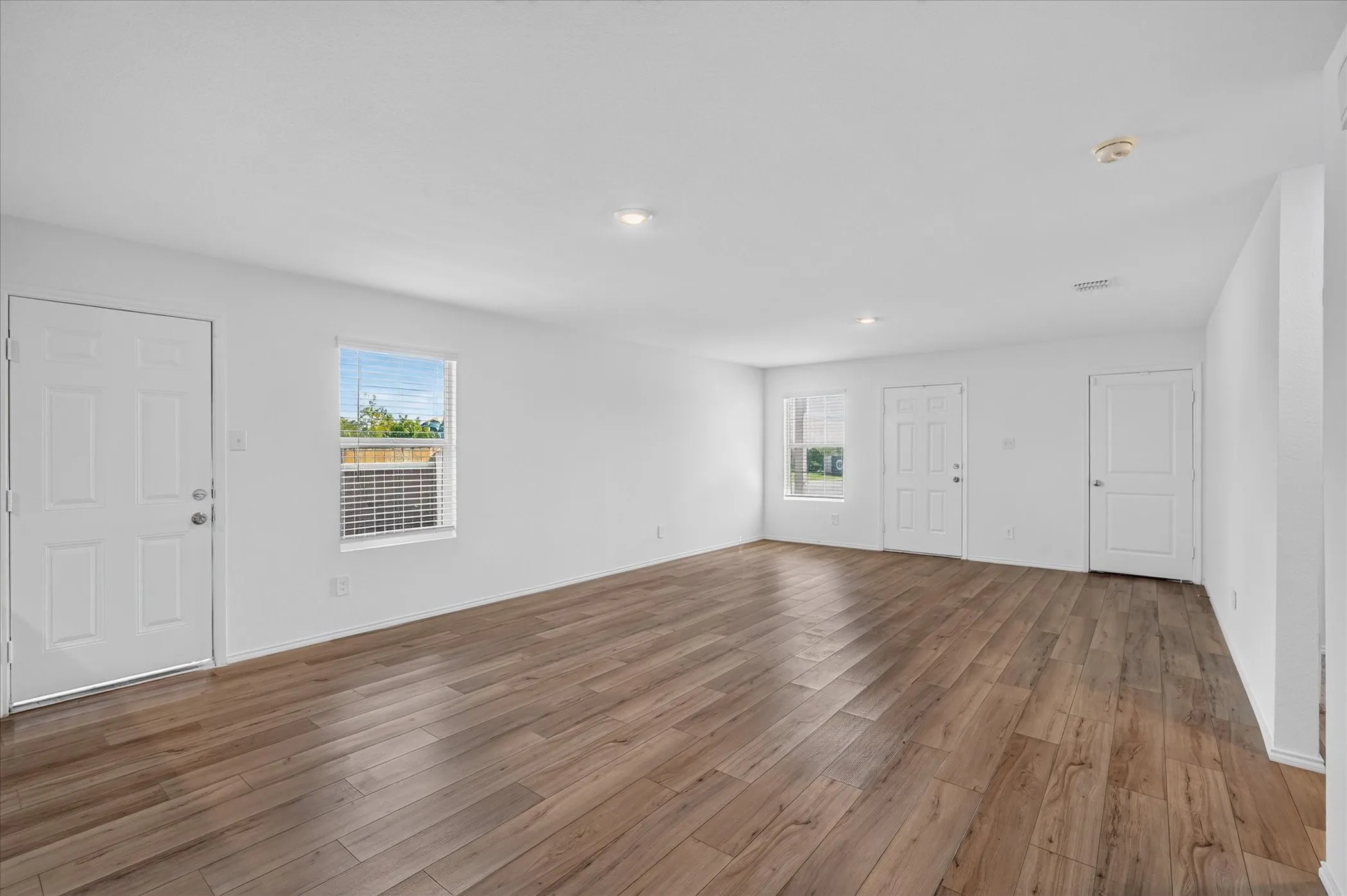 Spacious room featuring wood-finish flooring, multiple windows with blinds, recessed lighting, and white paneled doors