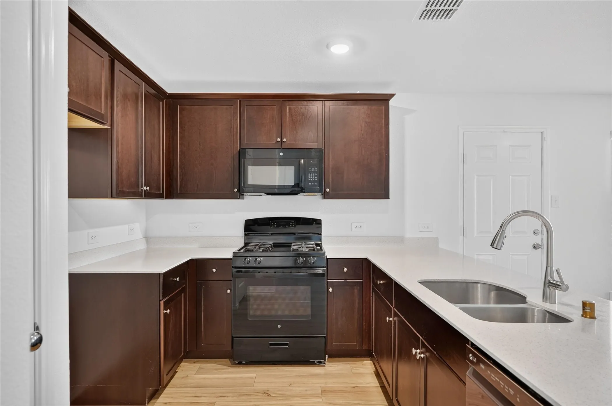 U-shaped kitchen featuring dark wood cabinetry, light-colored countertops, a black range with an oven, a built-in microwave, and wood-finish flooring