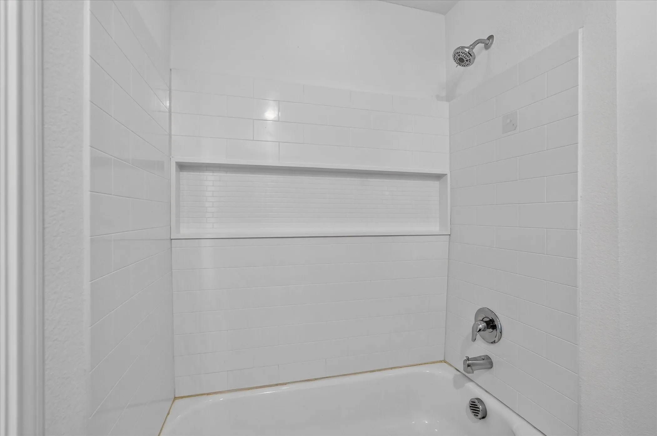 White subway tile shower surround with an integrated niche, chrome fixtures, and a white tub