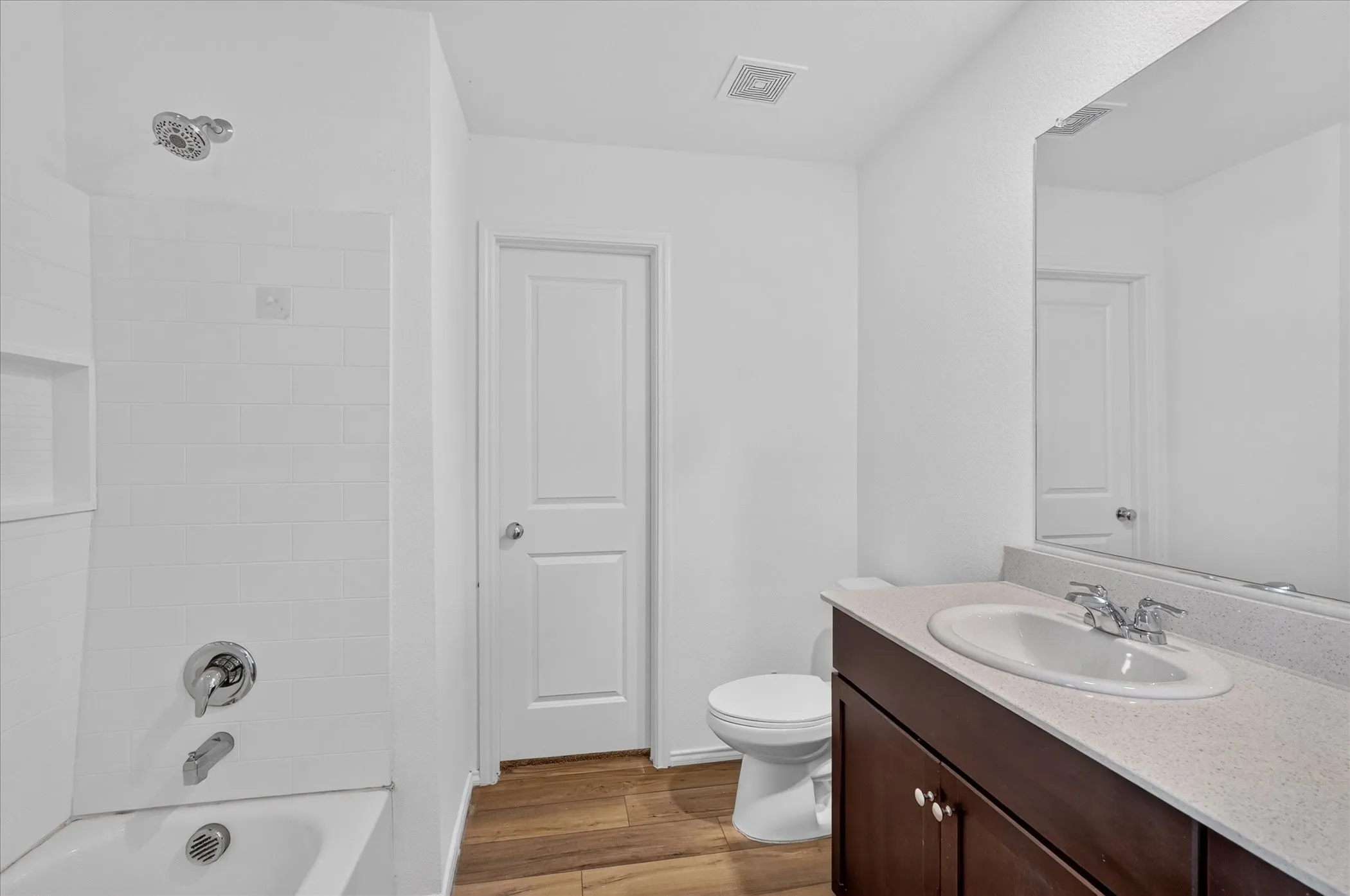Bathroom featuring a white subway tile tub surround, chrome fixtures, dark wood-finish vanity with an integrated sink, and wood-finish flooring
