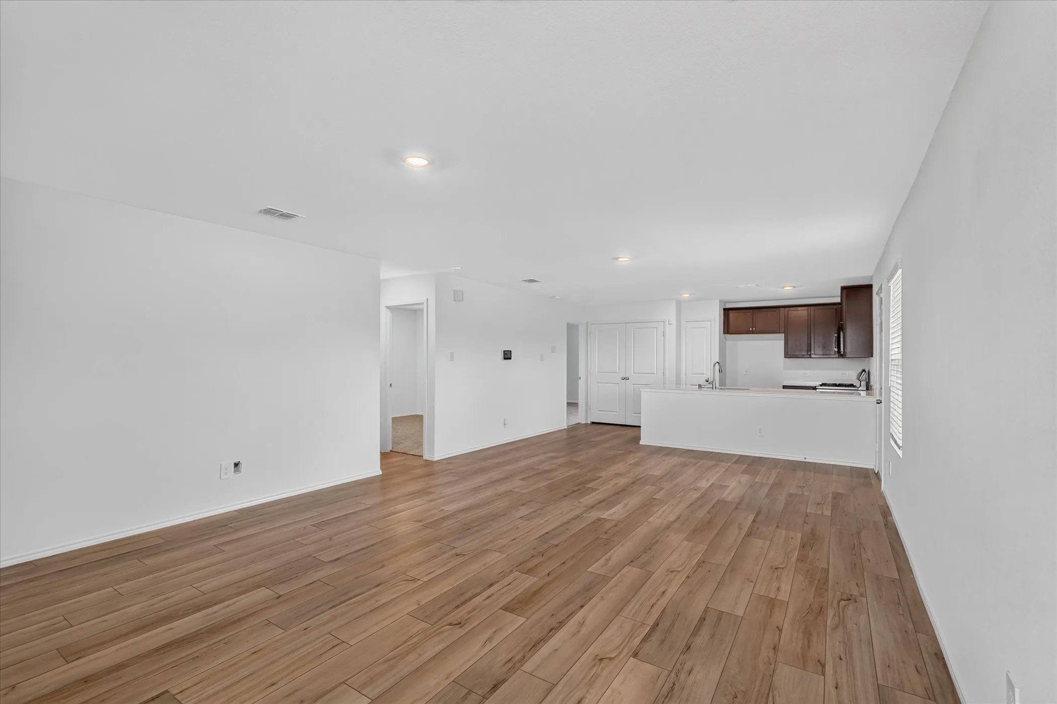 Wood-finish flooring throughout, recessed lighting, white walls, dark wood-finish cabinetry, and a white kitchen peninsula