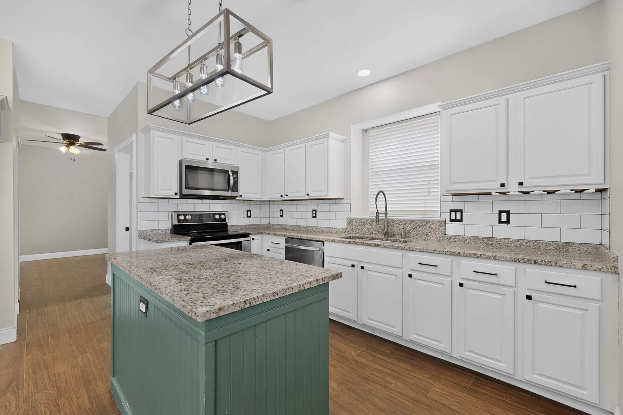 Kitchen featuring wood-finish flooring, an island with a contrasting base, white shaker-style cabinetry, stainless steel appliances, and a subway tile backsplash