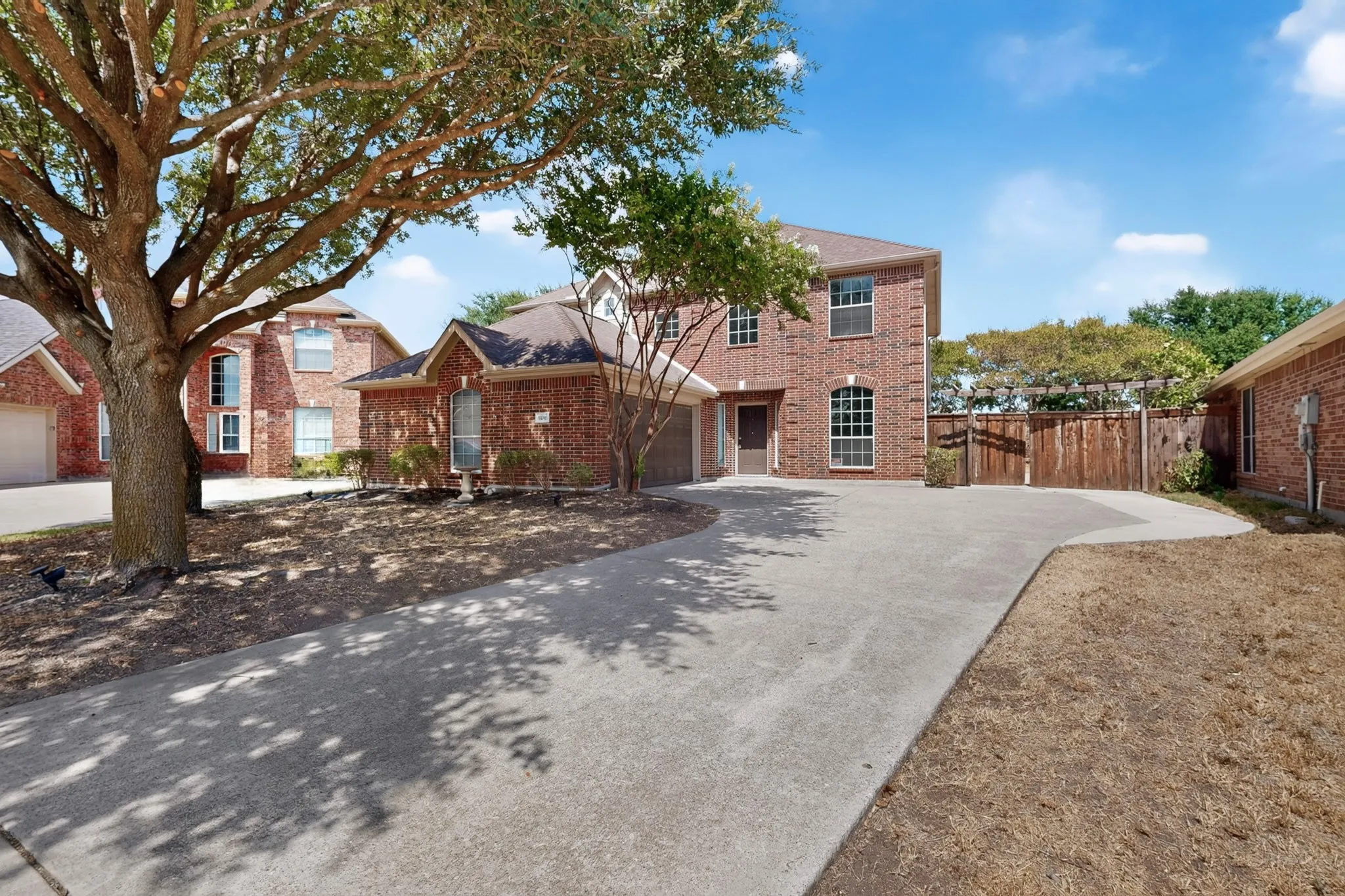 Two-story brick exterior with arched windows, mature trees, and a concrete driveway