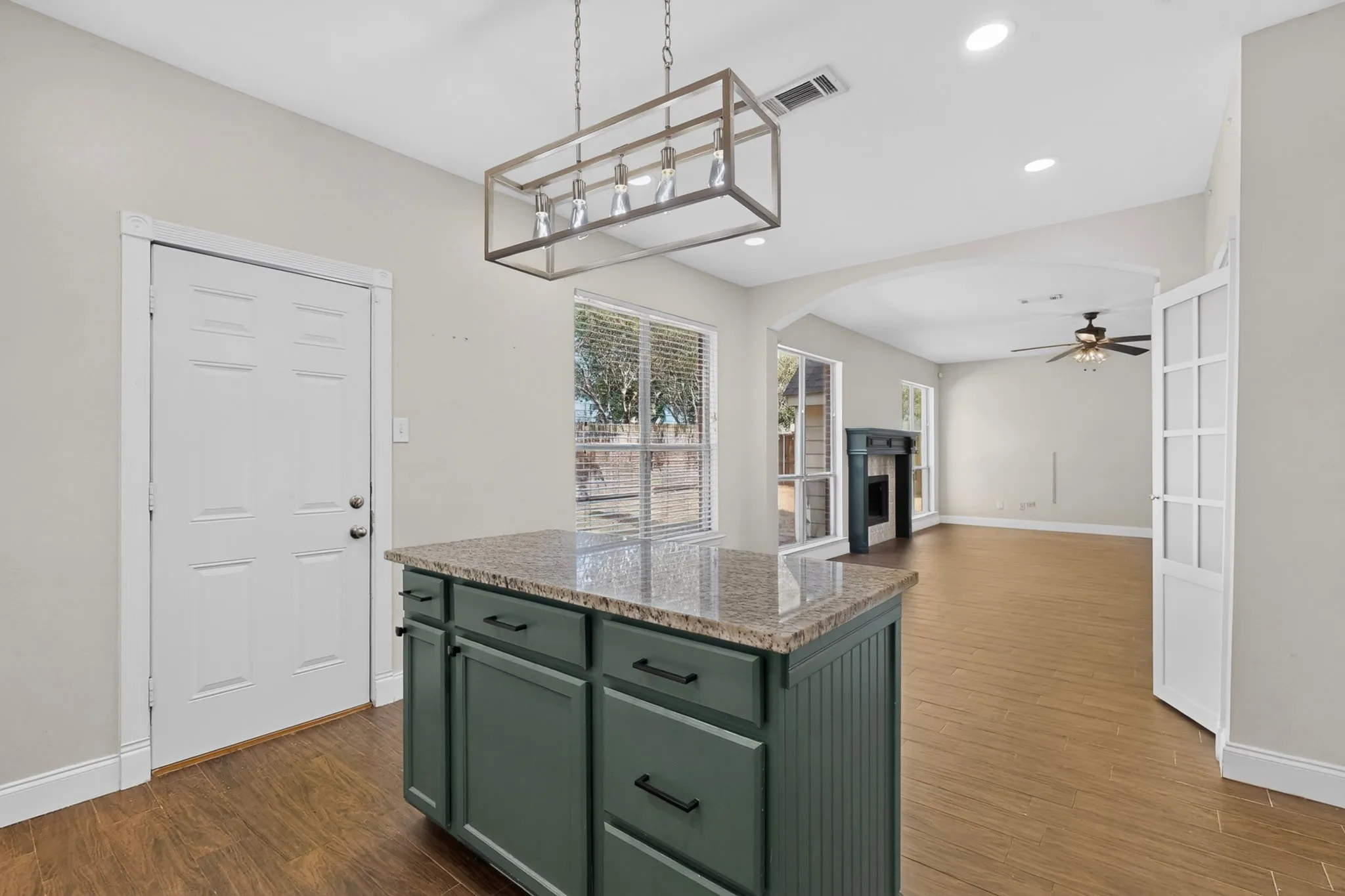 Kitchen island with granite countertop and green cabinetry, wood-finish flooring, and recessed lighting