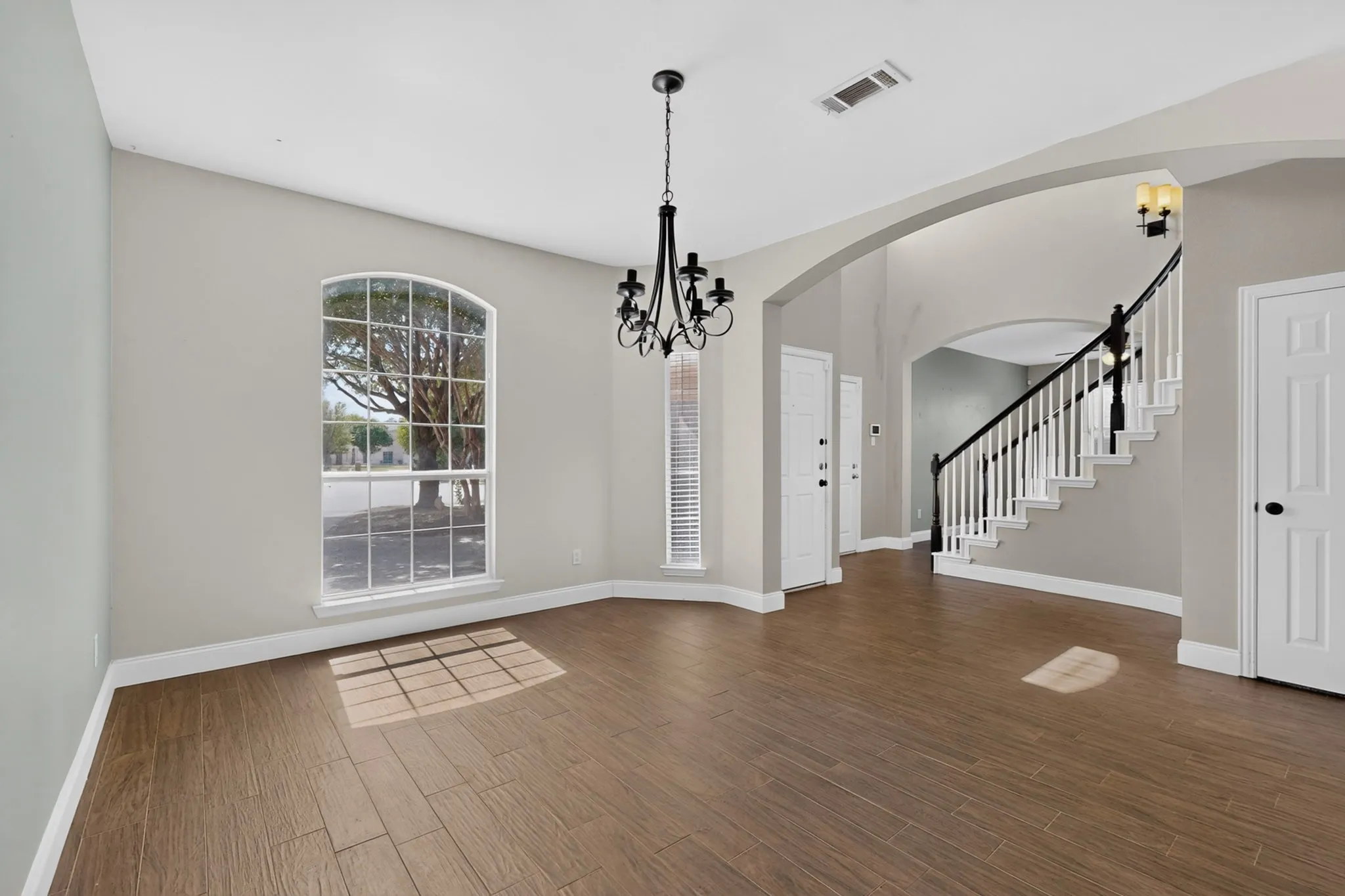 Wood-finish flooring, arched entryway, white spindle staircase with dark handrail, decorative chandelier, and arched window