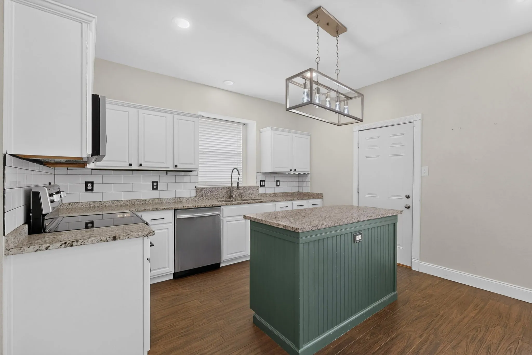 Kitchen featuring white cabinetry, subway tile backsplash, granite countertops, stainless steel appliances, and a central island with beadboard paneling
